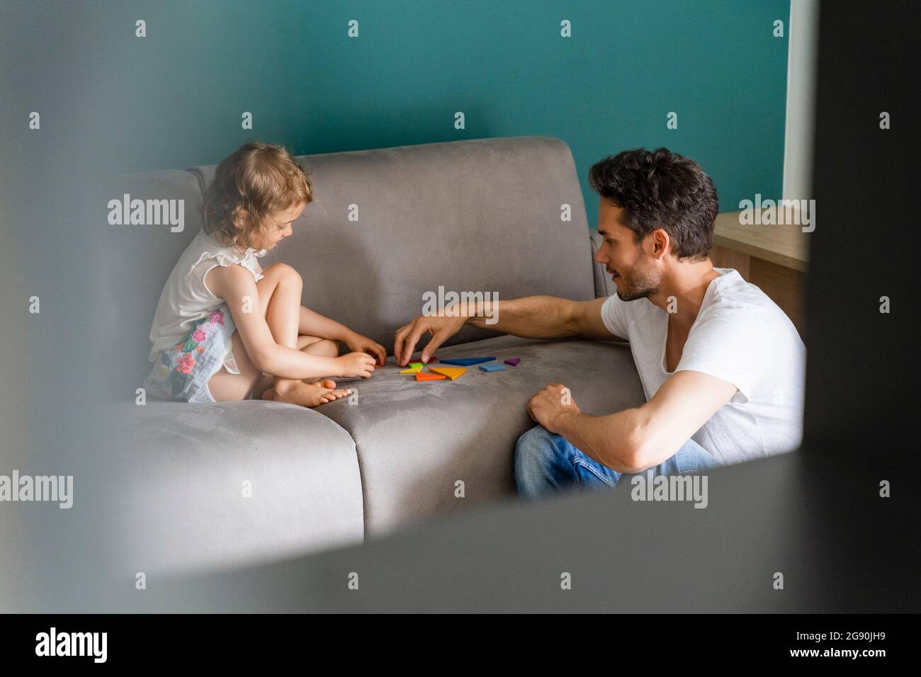 Father helping daughter while playing with puzzle on sofa Stock Photo