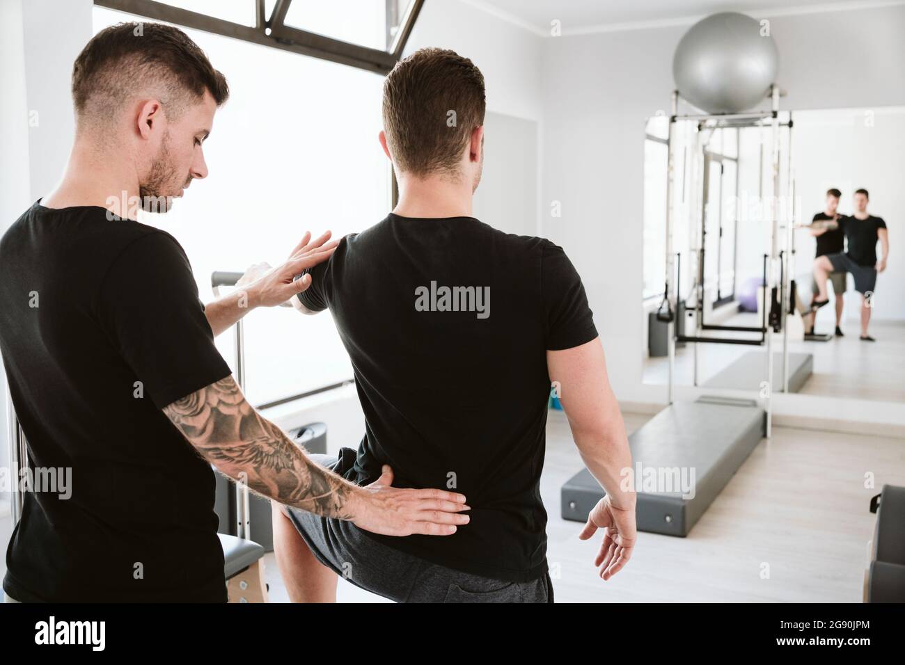 Male instructor providing support to man while exercising at pilates studio Stock Photo