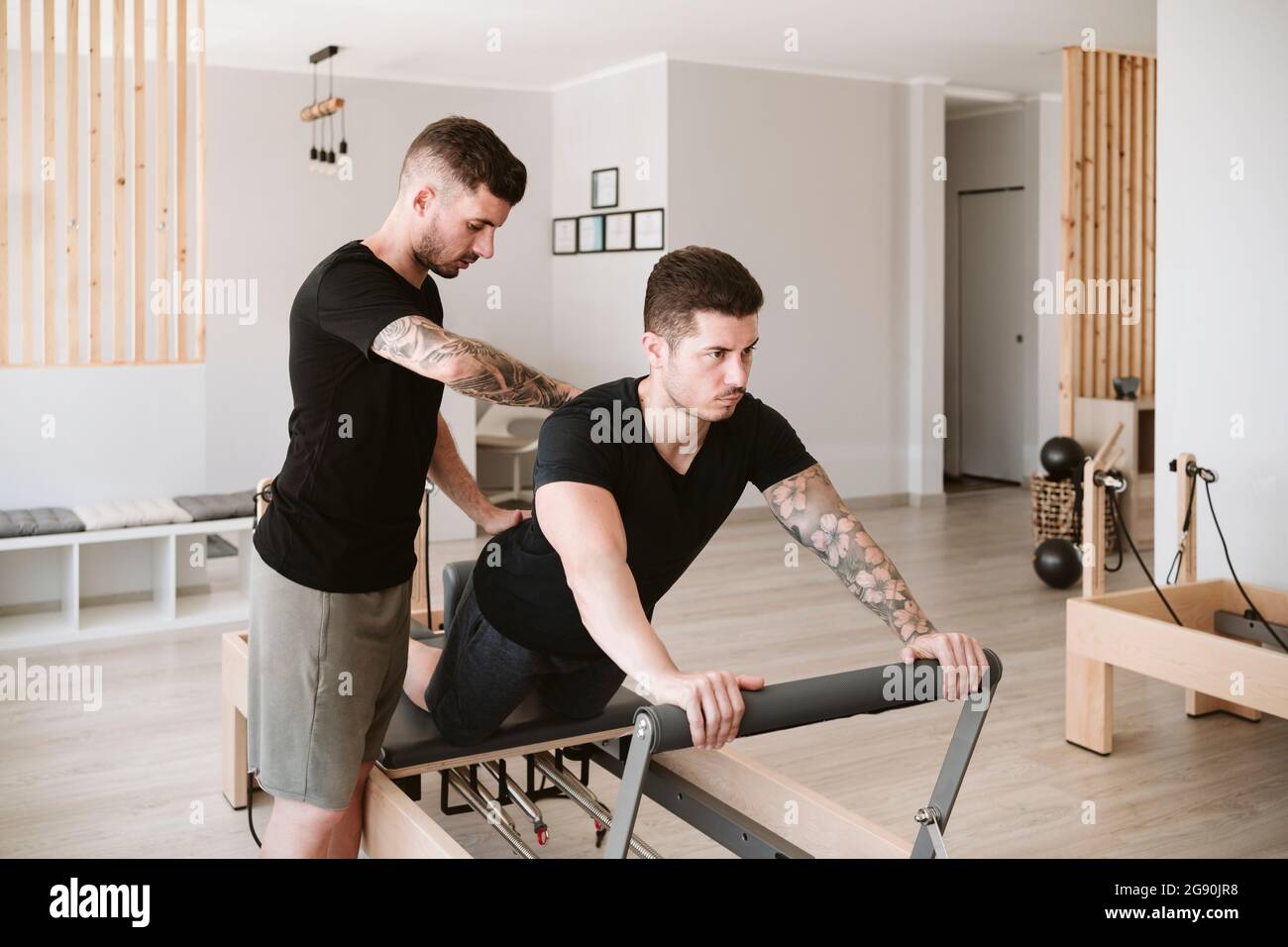 Male fitness trainer providing support while man practicing pilates in studio Stock Photo