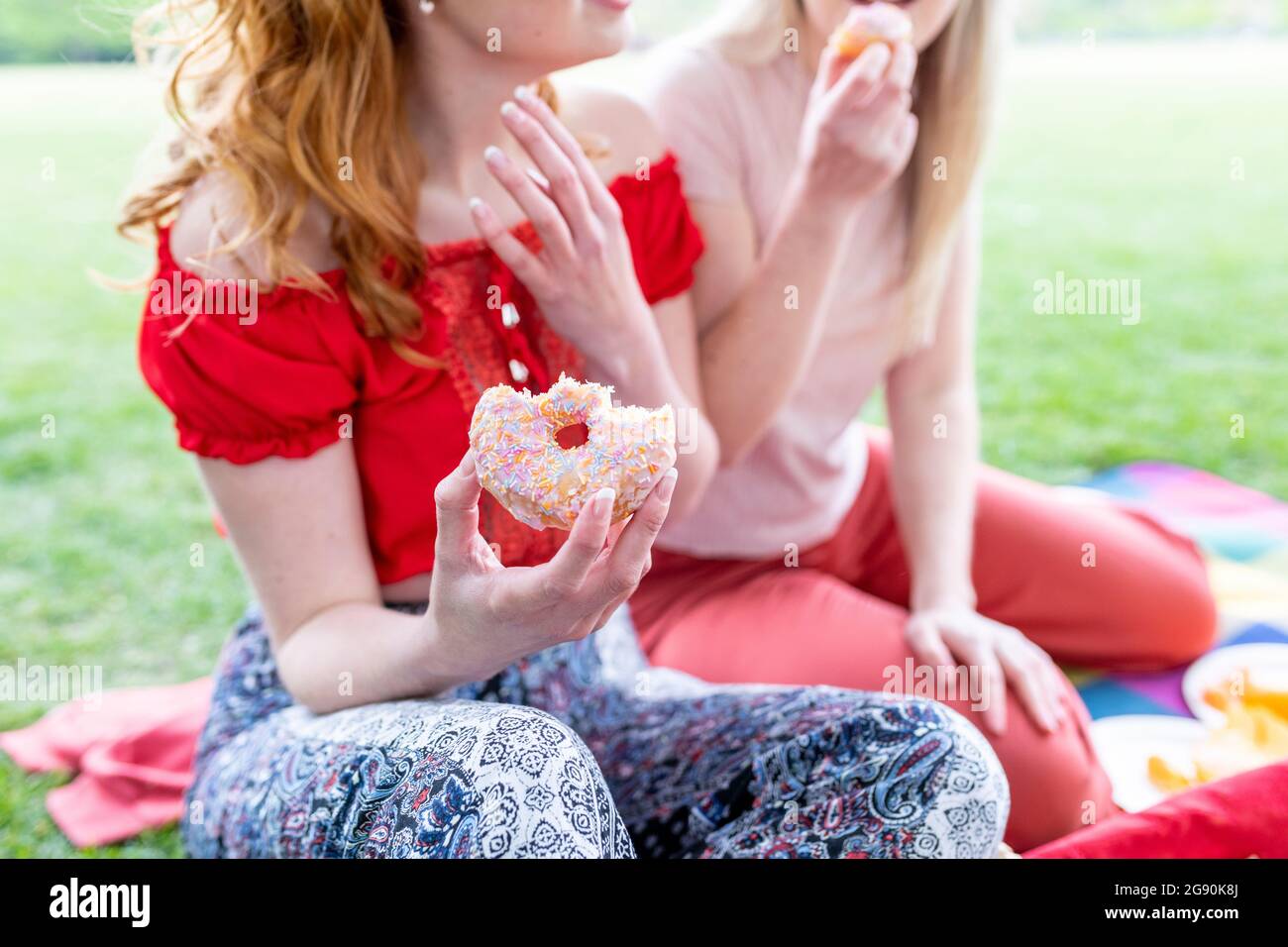 Woman holding doughnut while sitting with friend at park Stock Photo