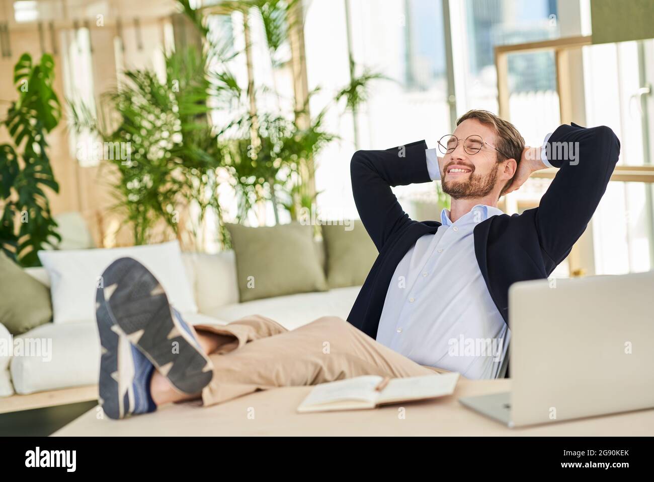Smiling relaxed male professional sitting with feet up on table in home