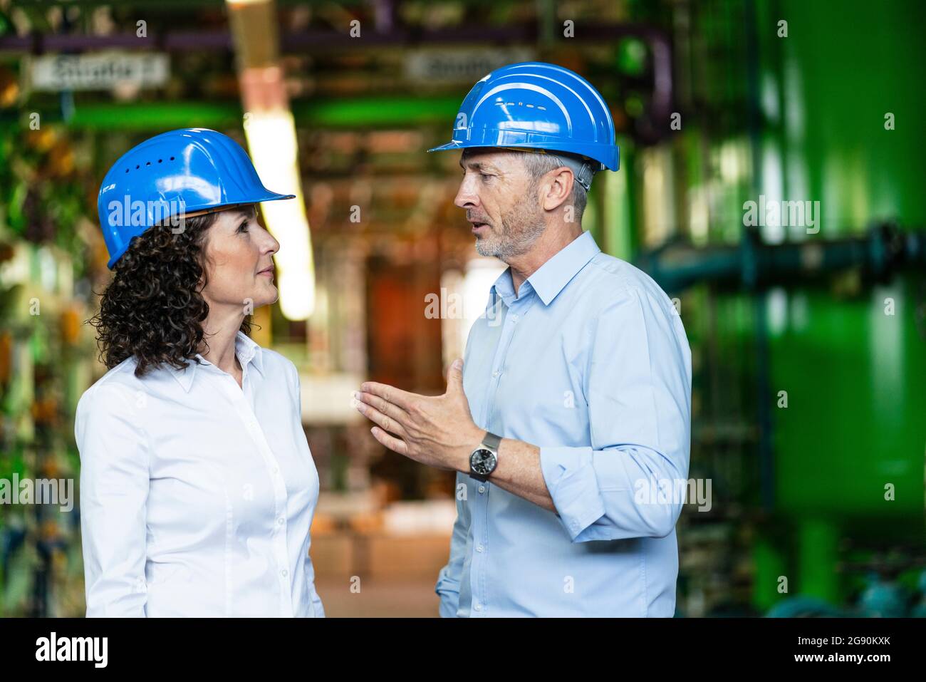 Male and female experts with hardhat having discussion while standing at power station Stock Photo