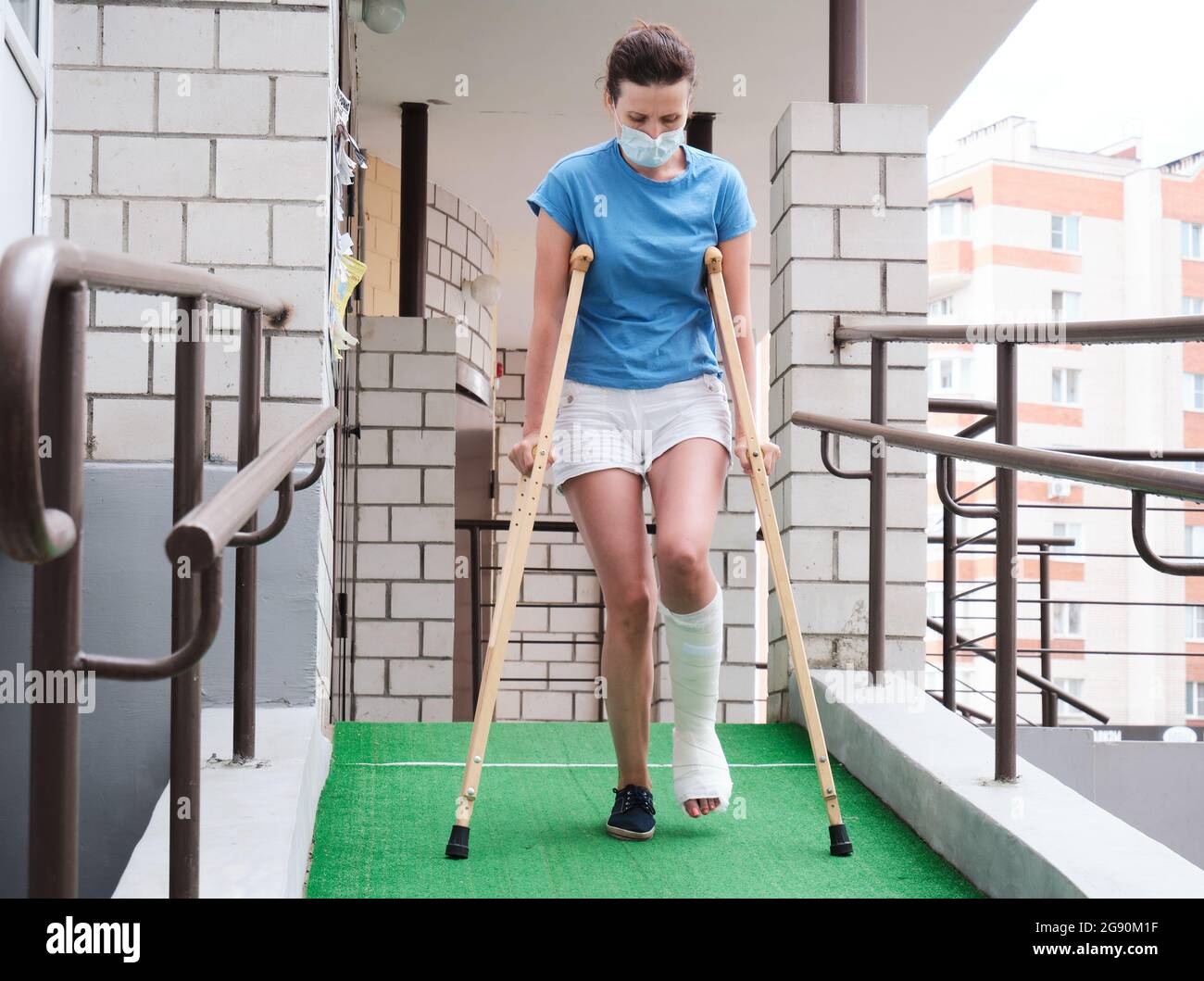 A woman with a broken leg walks down a ramp using orthopedic crutches. Stock Photo
