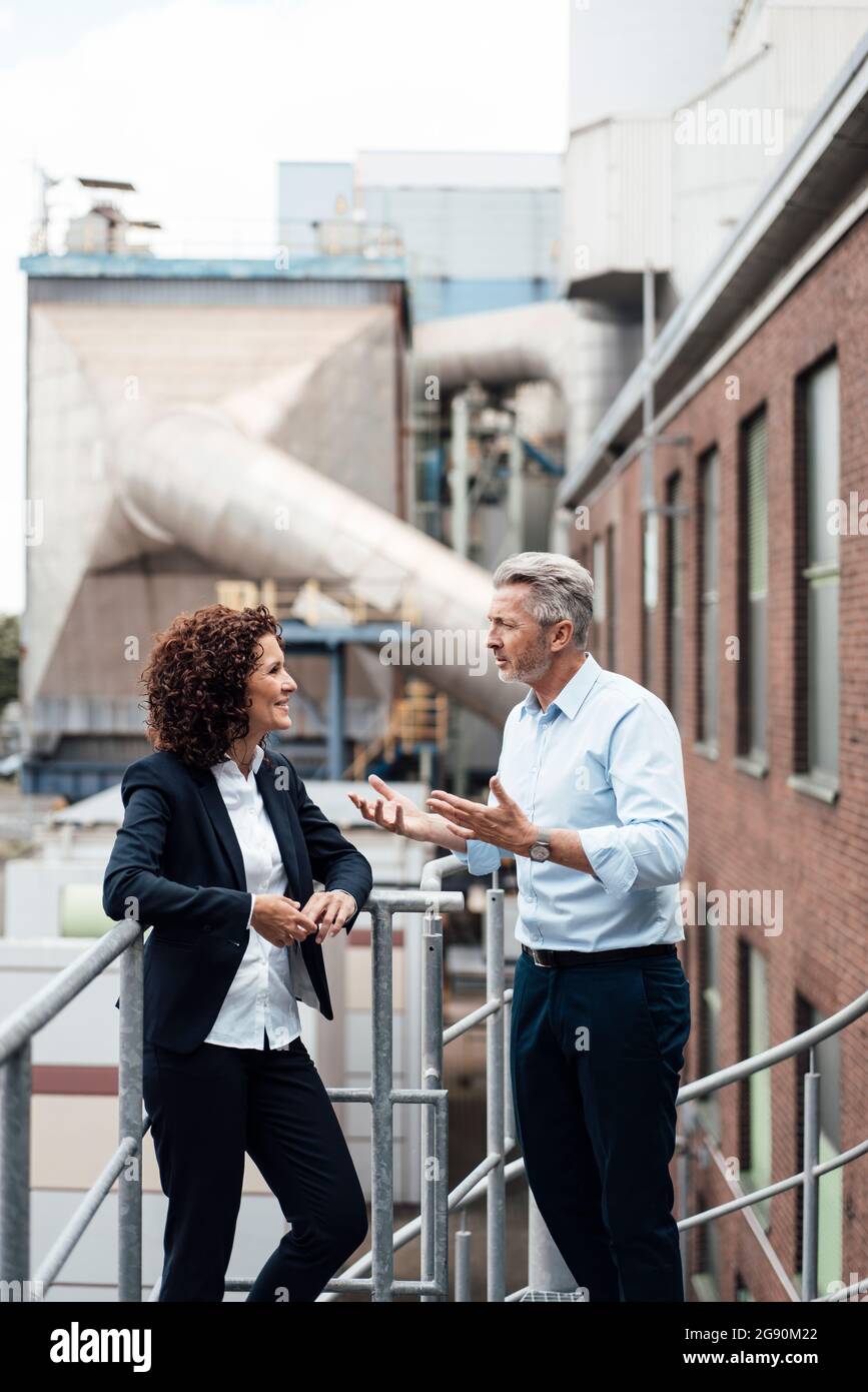 Male and female professionals having discussion while standing by railing Stock Photo