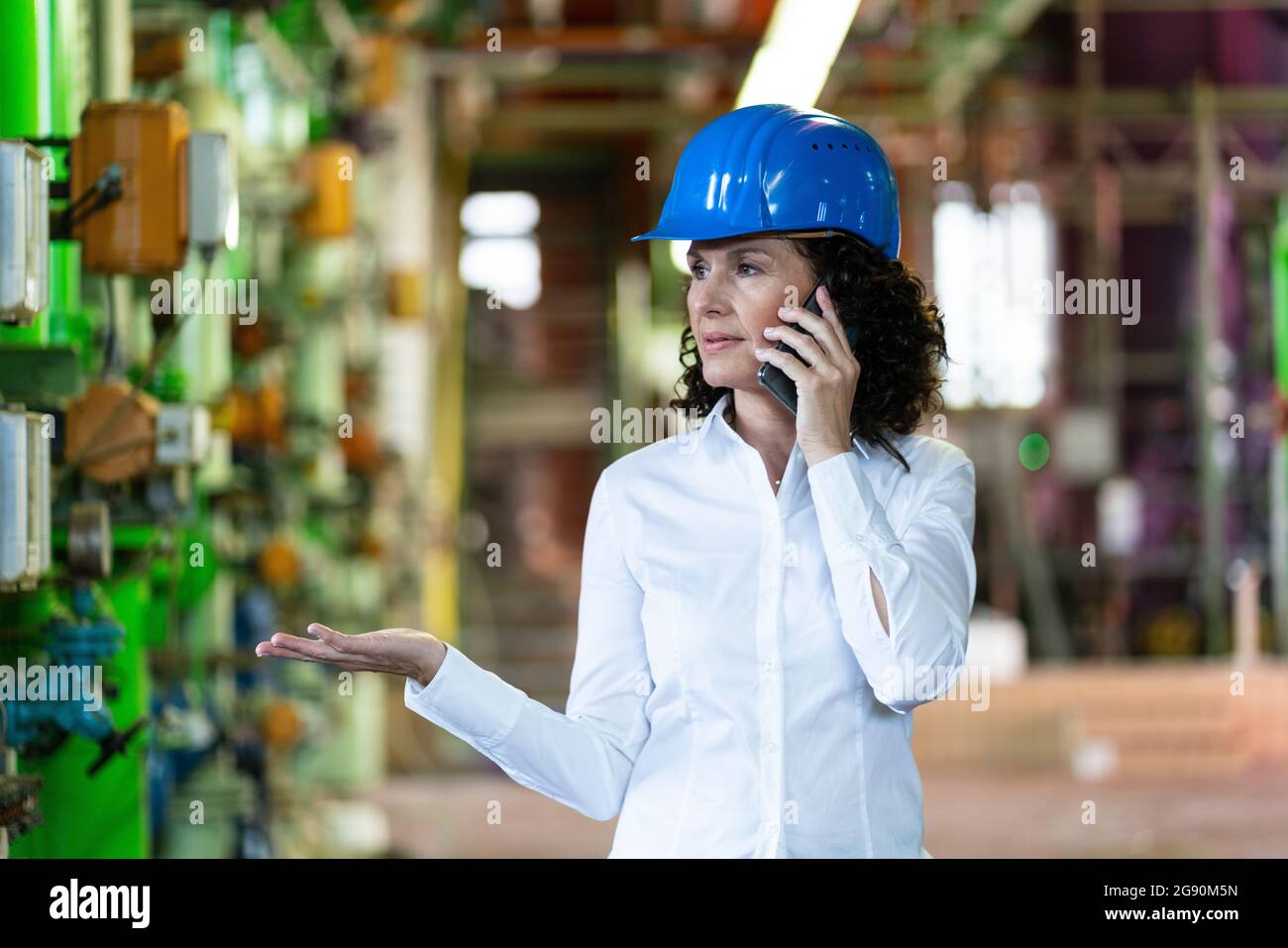 Female engineer with hardhat talking on mobile phone while standing at power station Stock Photo