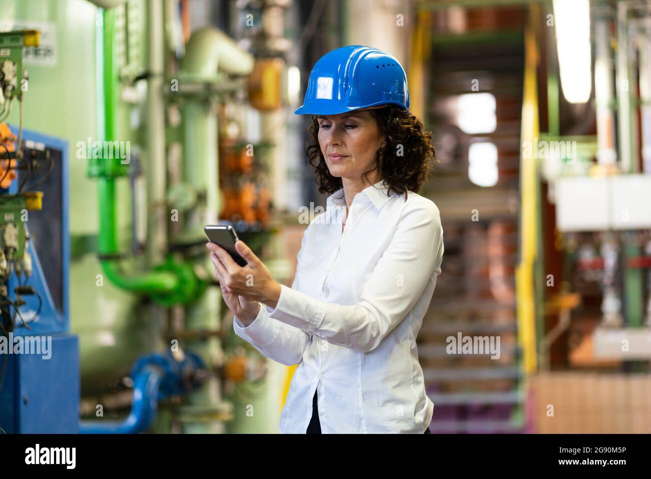 Female engineer with hardhat using mobile phone while standing in industry Stock Photo