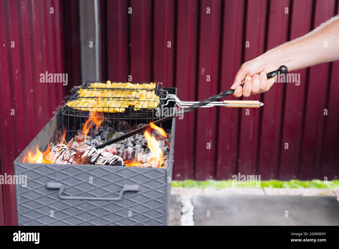 A man using a poker straightens the coals in the grill Stock Photo