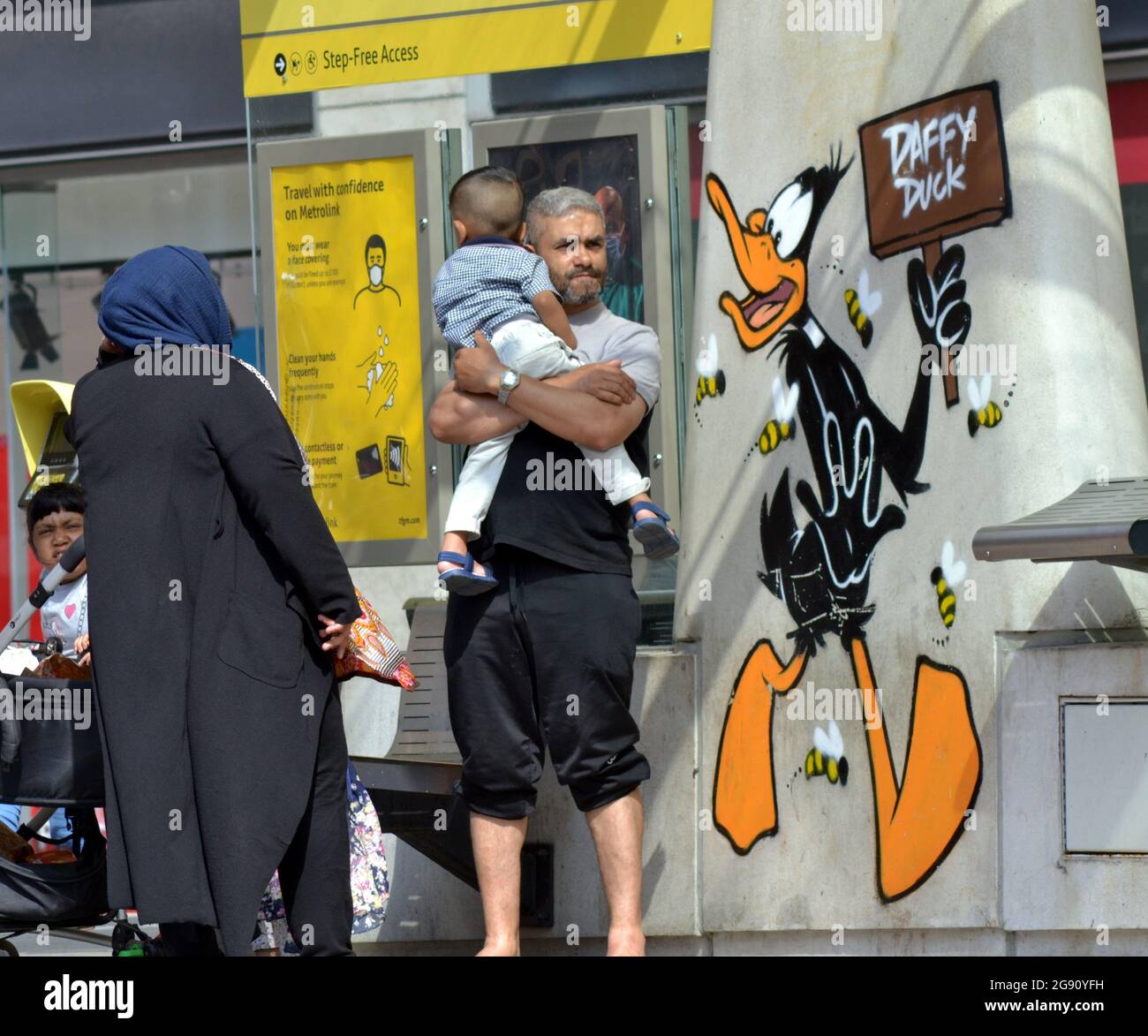 A man stands holding a baby next to an image of Daffy Duck cartoon character, part of a Looney Tunes art trail which has opened in Manchester, England. Stock Photo