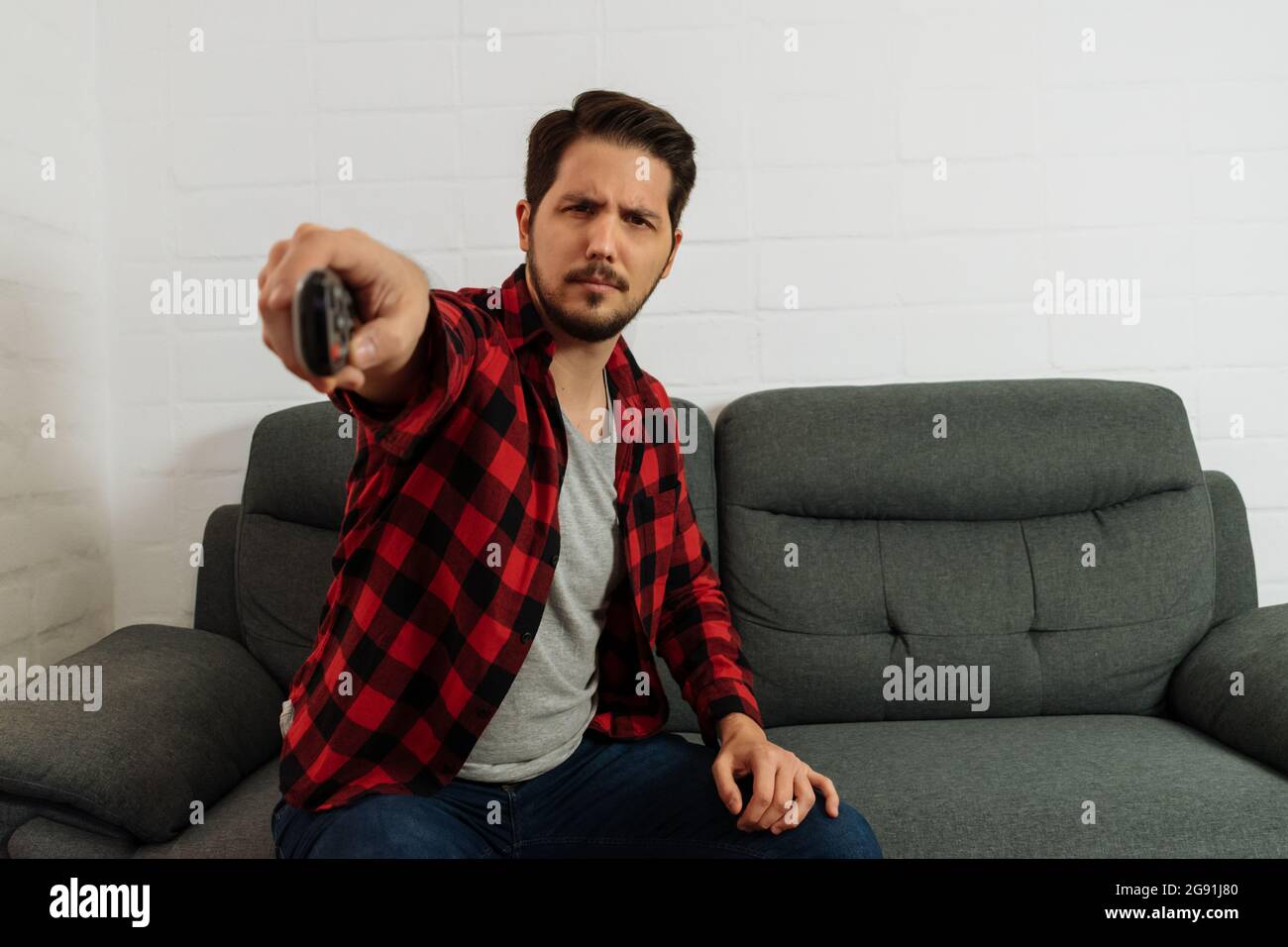 latin man with expression of concentration changing channel with remote control Stock Photo