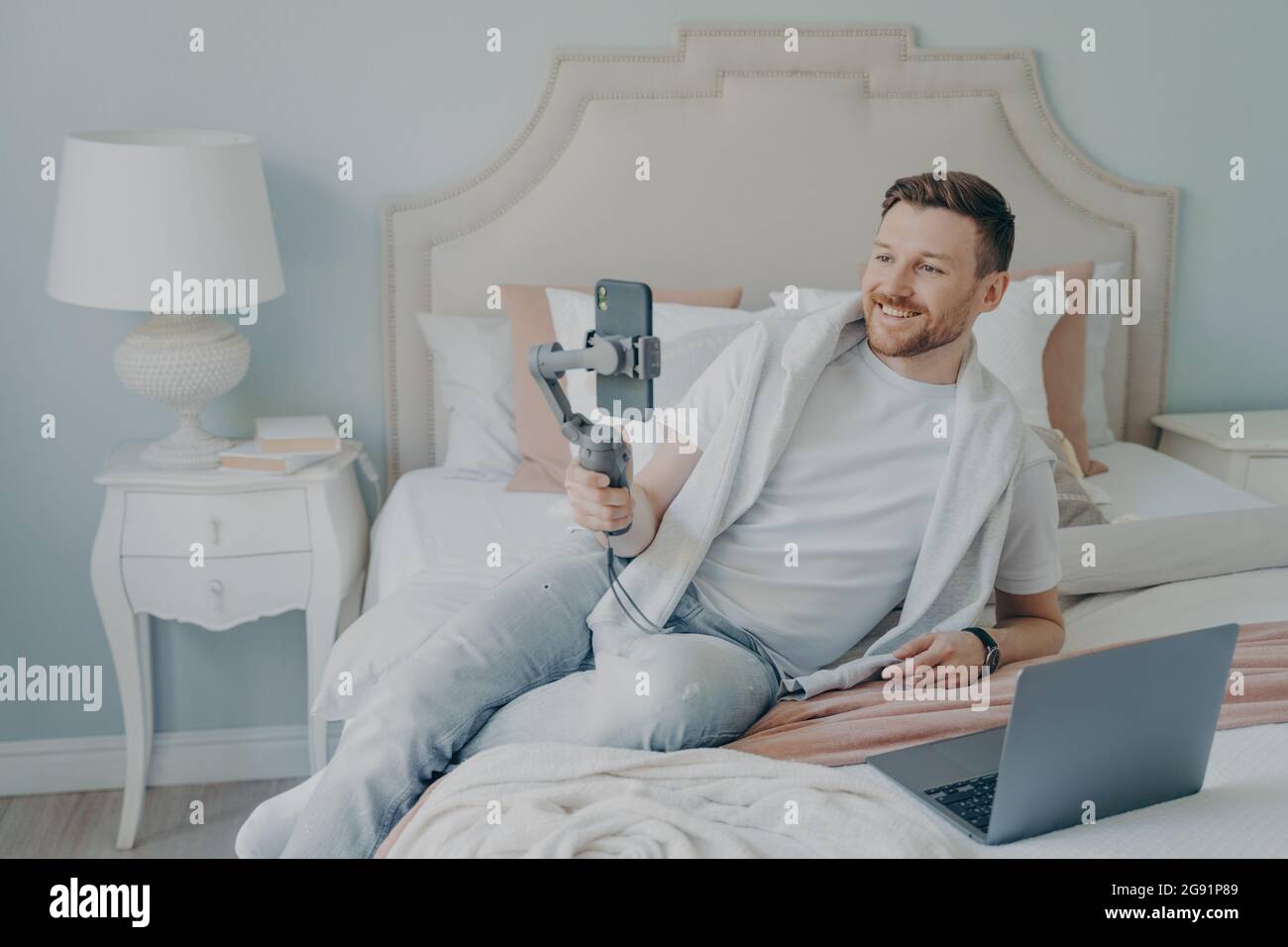 Young man lying on bed while video chatting using phone Stock Photo