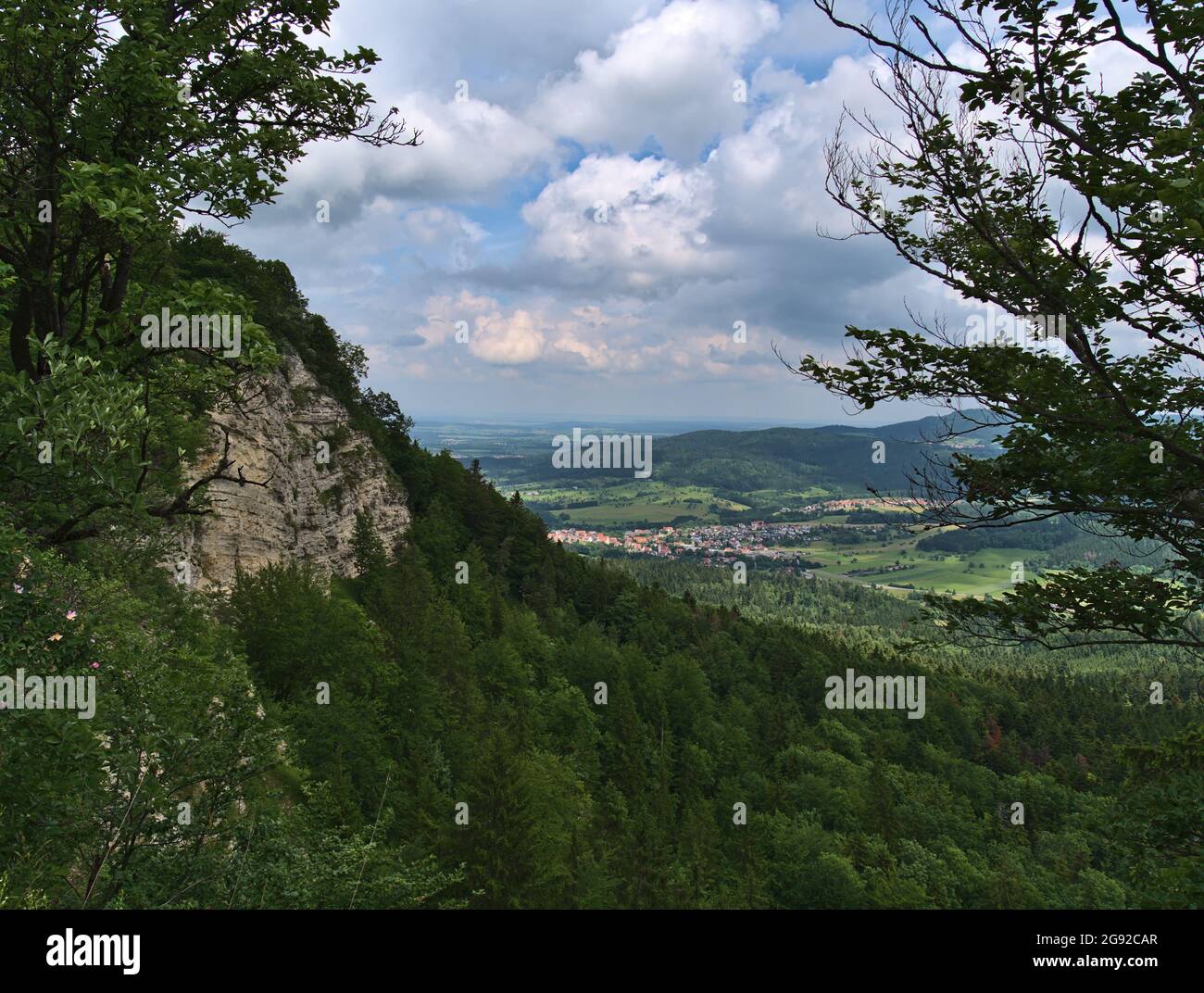 Rock face at the edge ('Albtrauf') of low mountain range Swabian Alb viewed through trees with green forests and the eastern part of town Balingen. Stock Photo