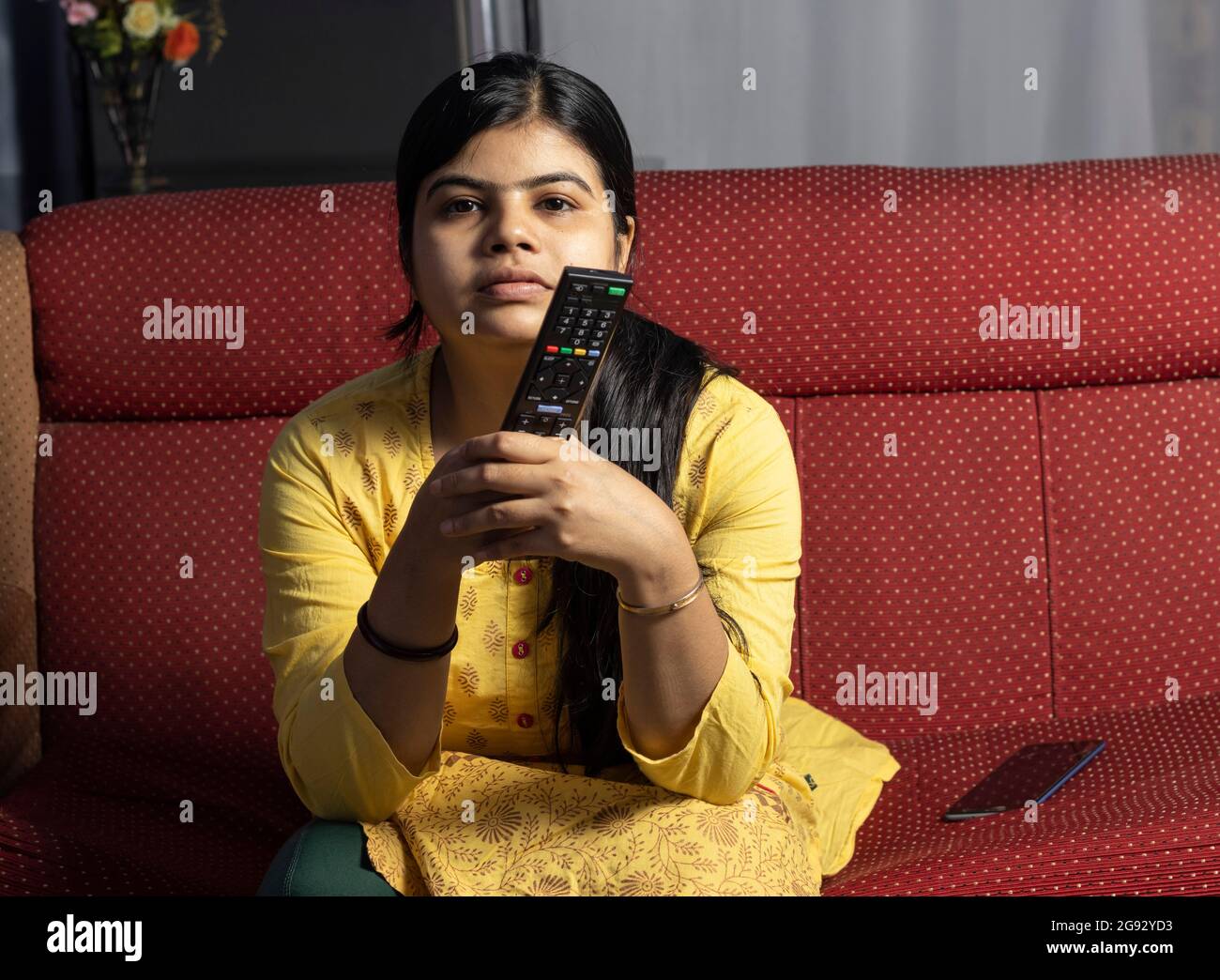 An Indian housewife woman watching television immersively holding remote in hand Stock Photo