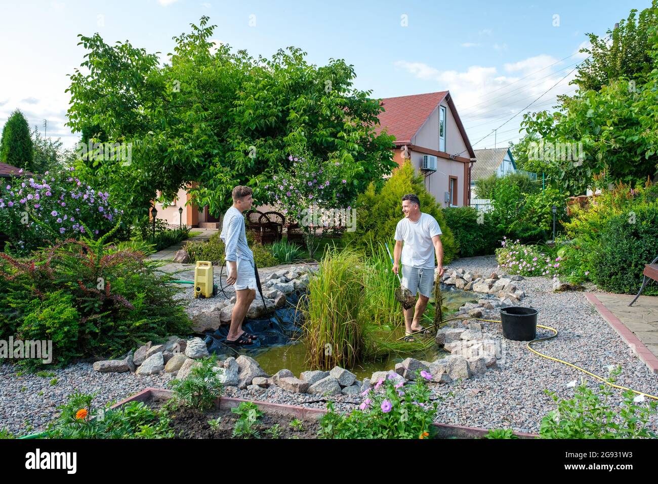 Father and son cleaning garden pond bottom with highpressure washer