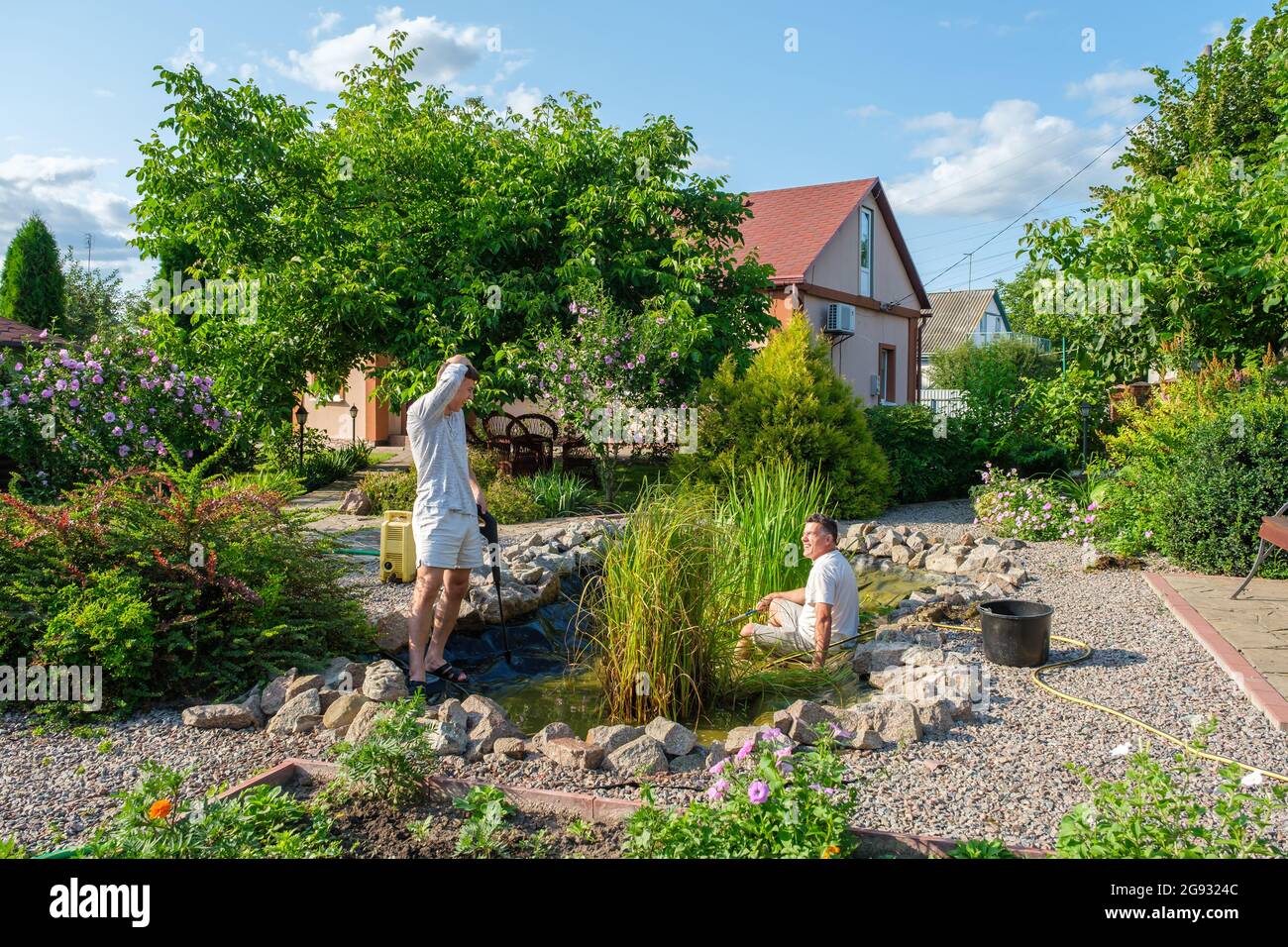 Father and son cleaning garden pond bottom with highpressure washer