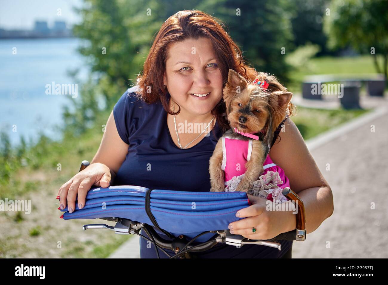 Overweight smiling female with yorkshire terrier in hands in garden. Stock Photo