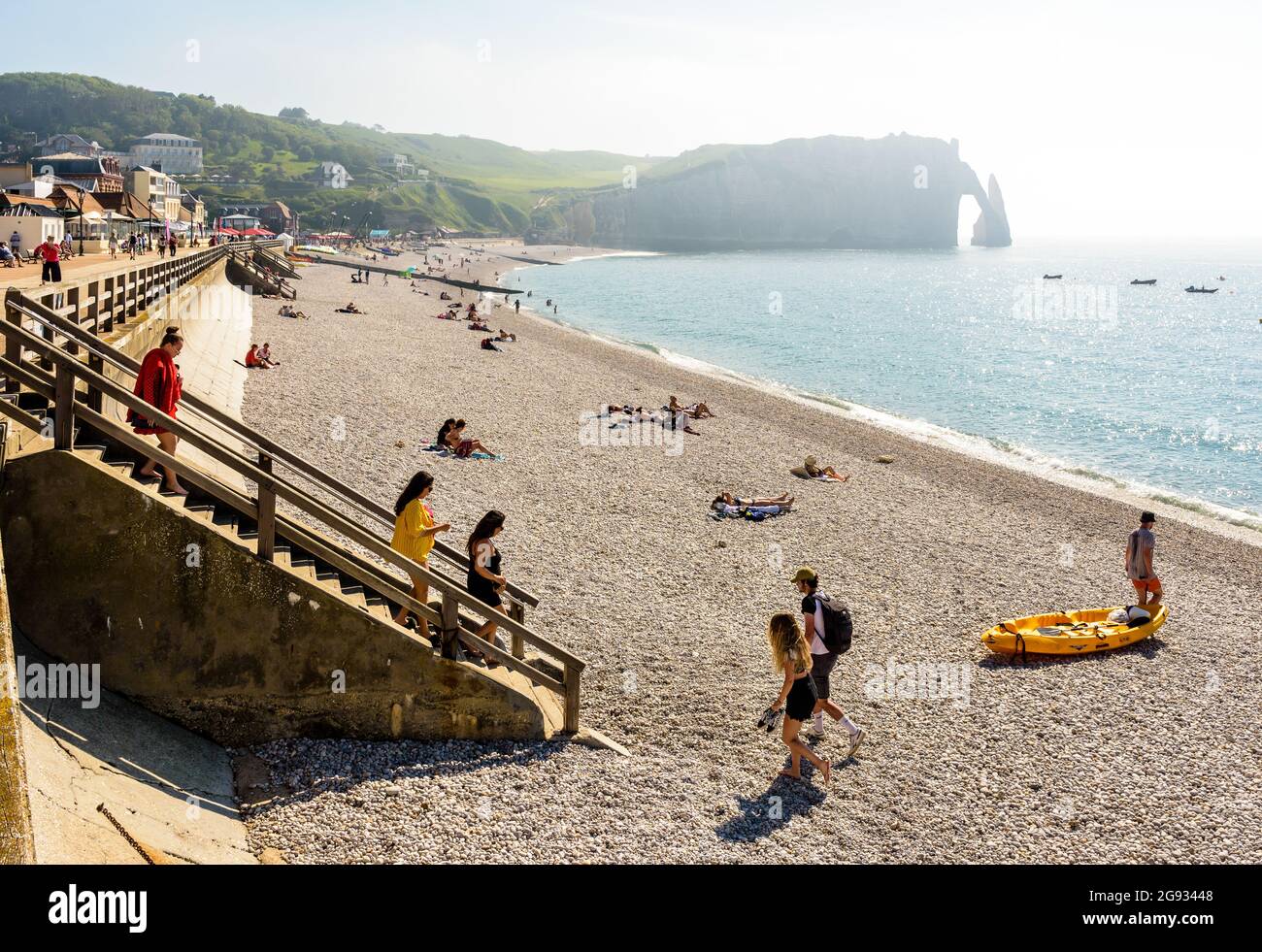 Tourists enjoying the pebble beach in Etretat, Normandy, with the Aval cliff, its arch and the Needle in the distance. Stock Photo