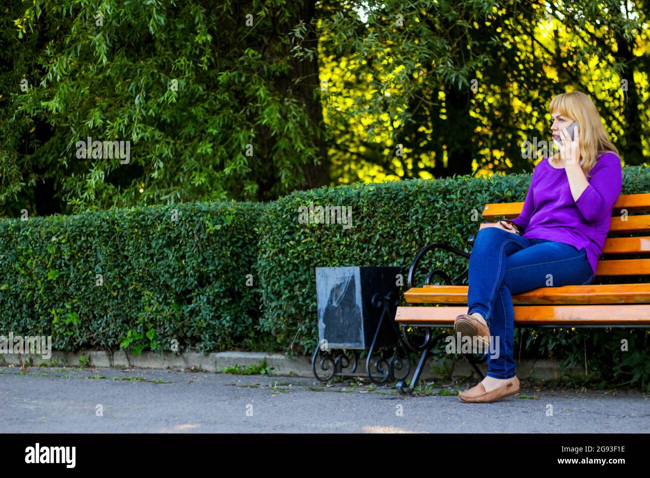Defocus caucasian blond woman talking, speaking on the phone outside,  outdoor. 40s years old woman in purple blouse in park on bench. Adult  female Stock Photo - Alamy