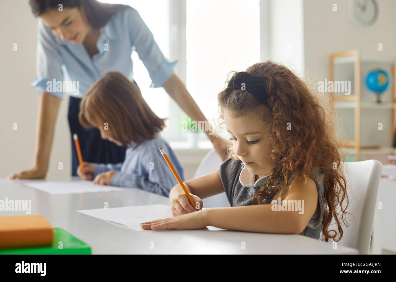 Close up of little schoolgirl intently writing or drawing while sitting at a desk in class. Stock Photo