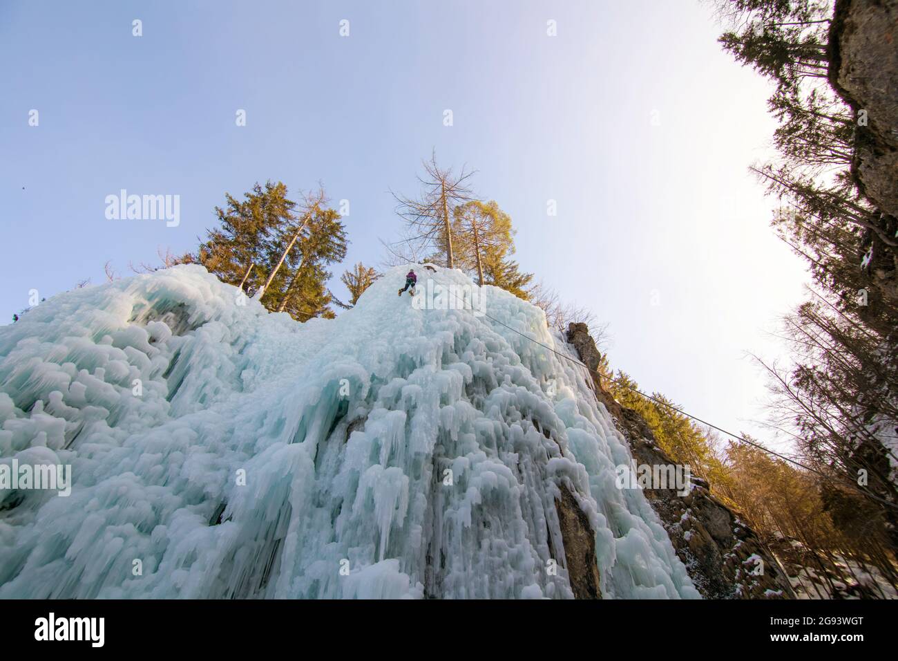 Female ice climber going down an ice waterfall, using a safety top rope ...