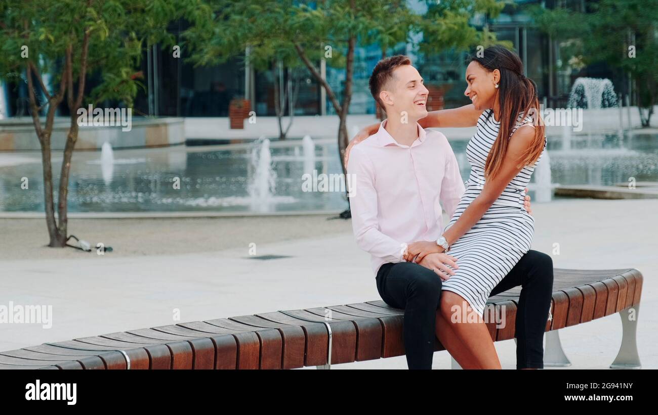 Young mixed-race family having nice time outdoors: laughing, hugging and talking to each other. The fountains are in the background. Stock Photo
