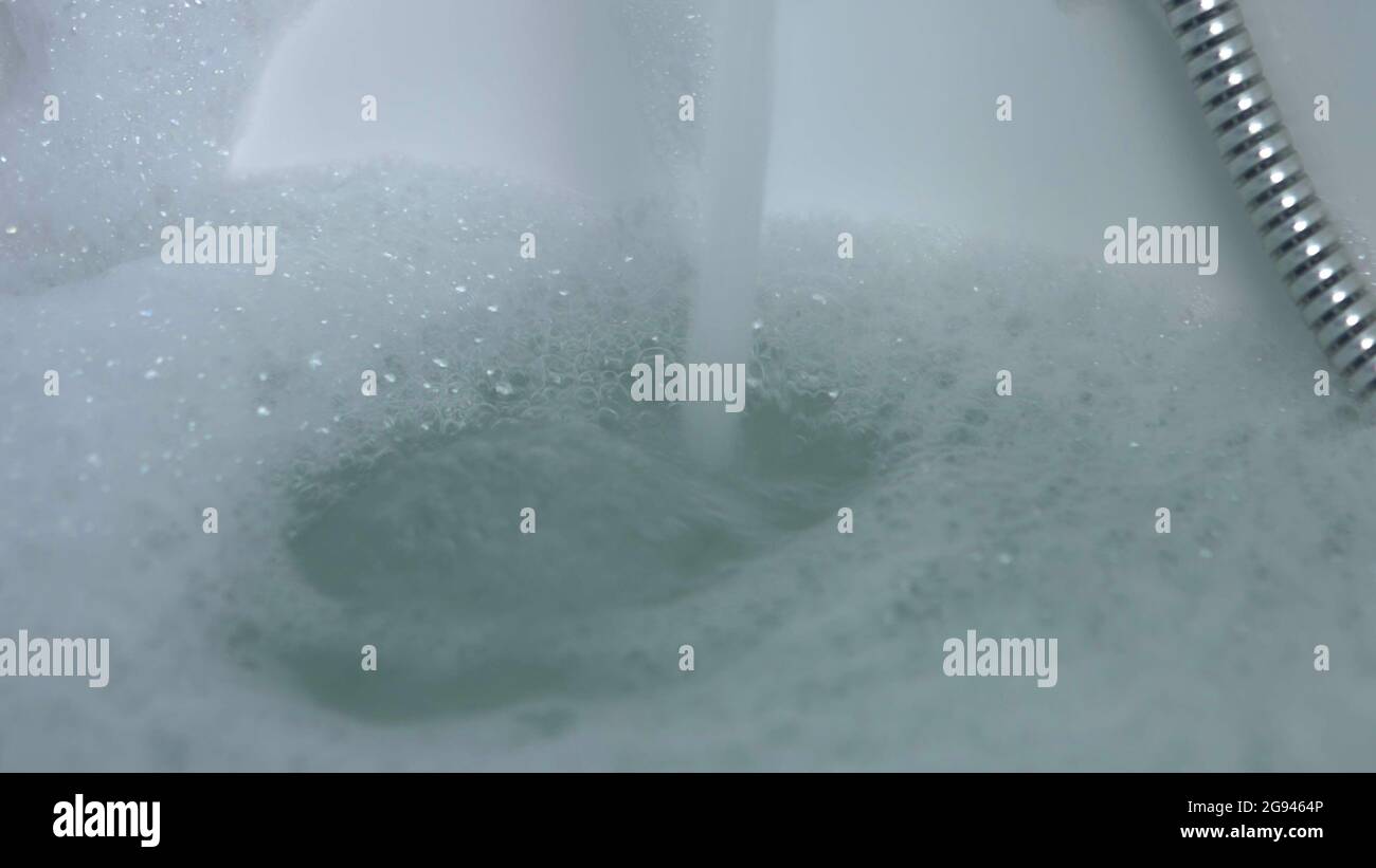 Water falling in to the bathtub from tap. Bath with bubbles. Slowmotion