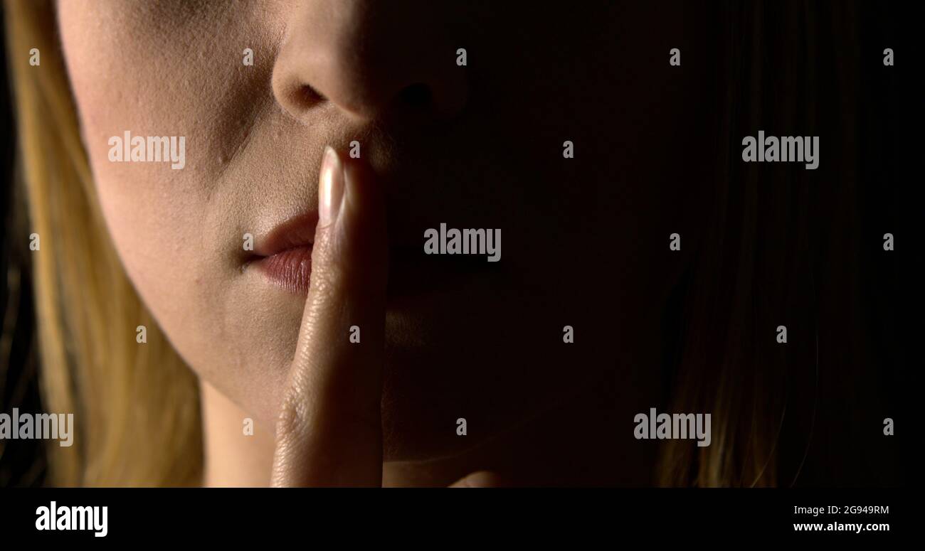 Woman putting finger on mouth. She is showing hush silence sign. Stock Photo