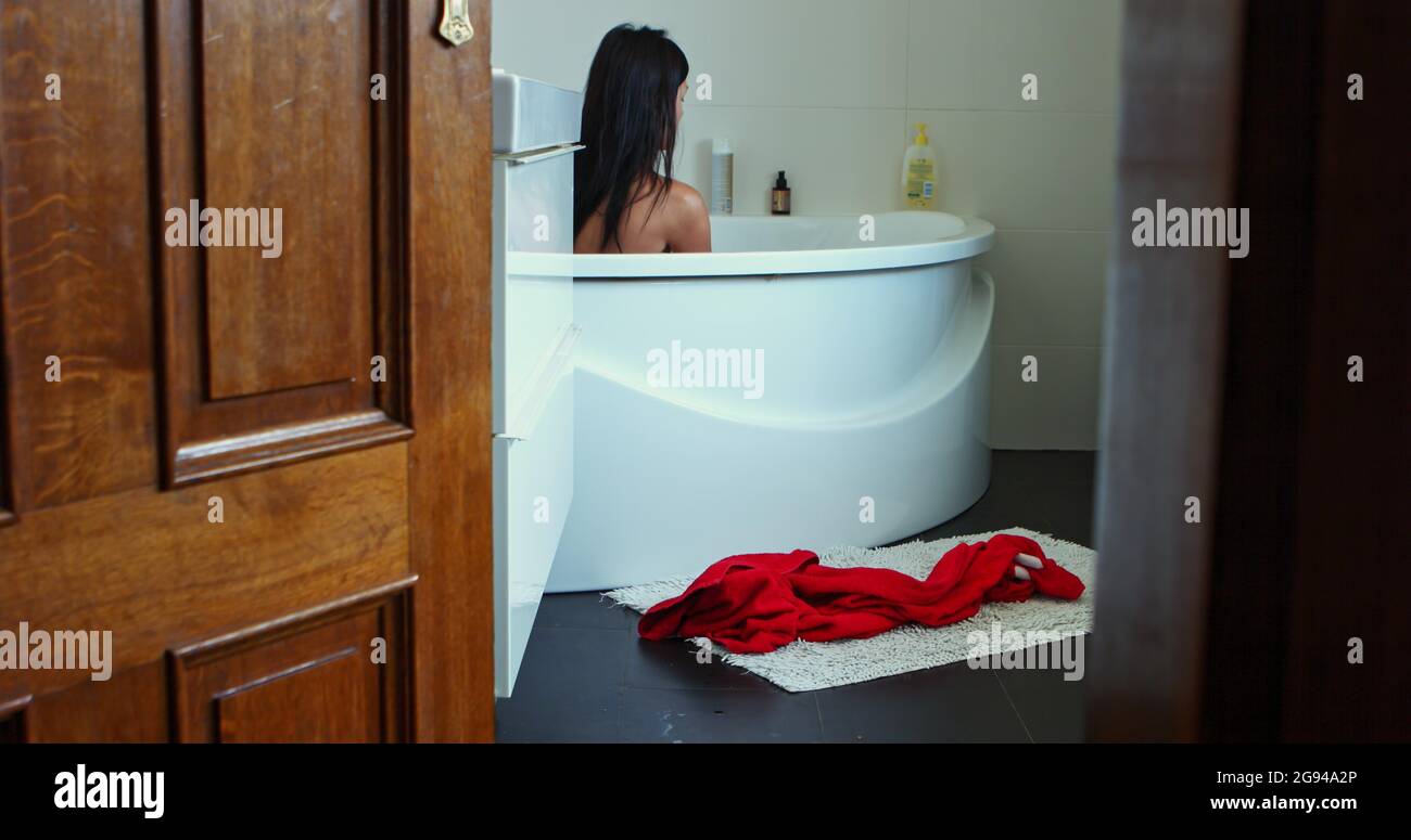Woman taking a bath at her home bathroom. View through the opened doors. Stock Photo