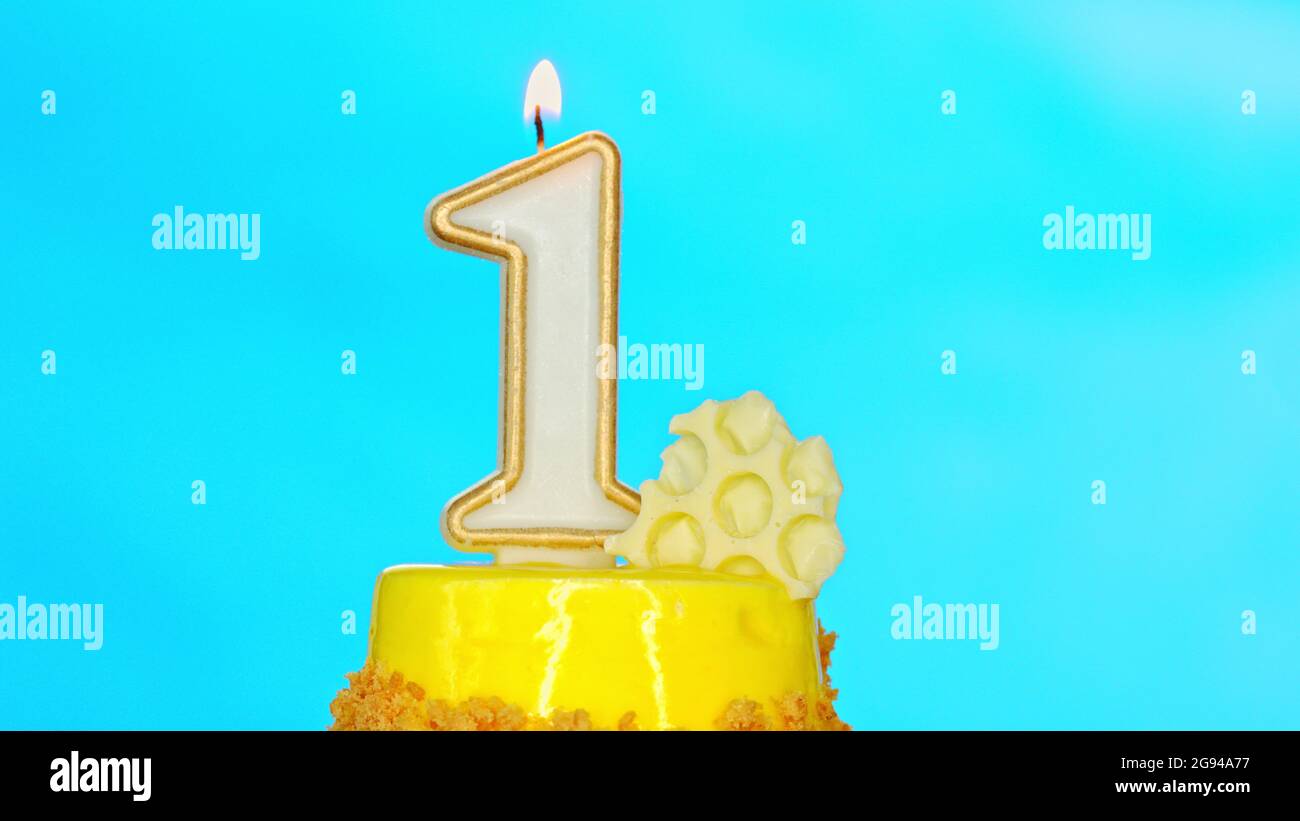 Yellow cupcake with one candle for first birthday on blue background. Stock Photo
