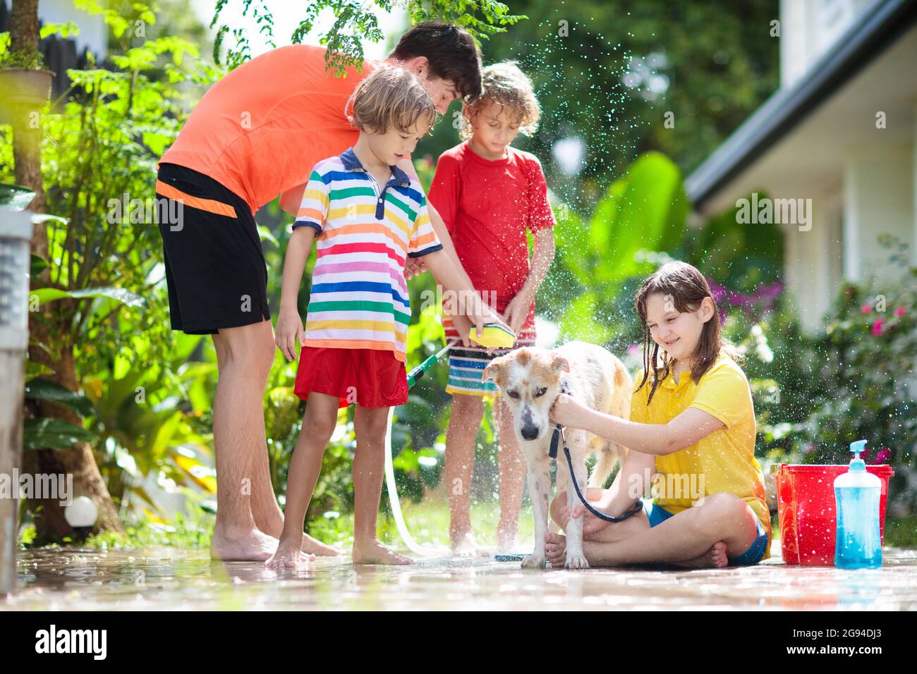 Kids wash dog in summer garden. Water hose and sprinkler fun for kid