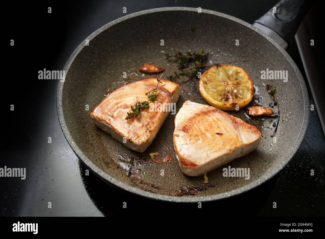 Tuna steaks n a frying pan with lemon, garlic and thyme on a back stove