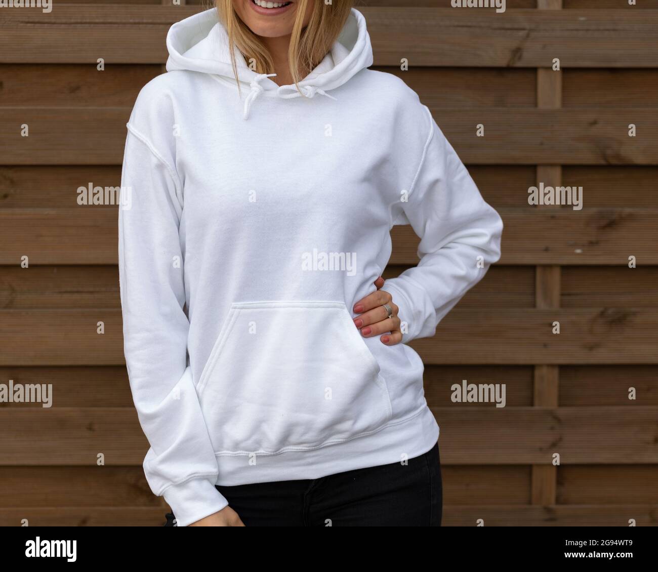 Blond unrecognizable woman wears white hoodie, she stands in front of camera. The empty space on her blouse in for design or inscription, for clothing mockup. Stock Photo