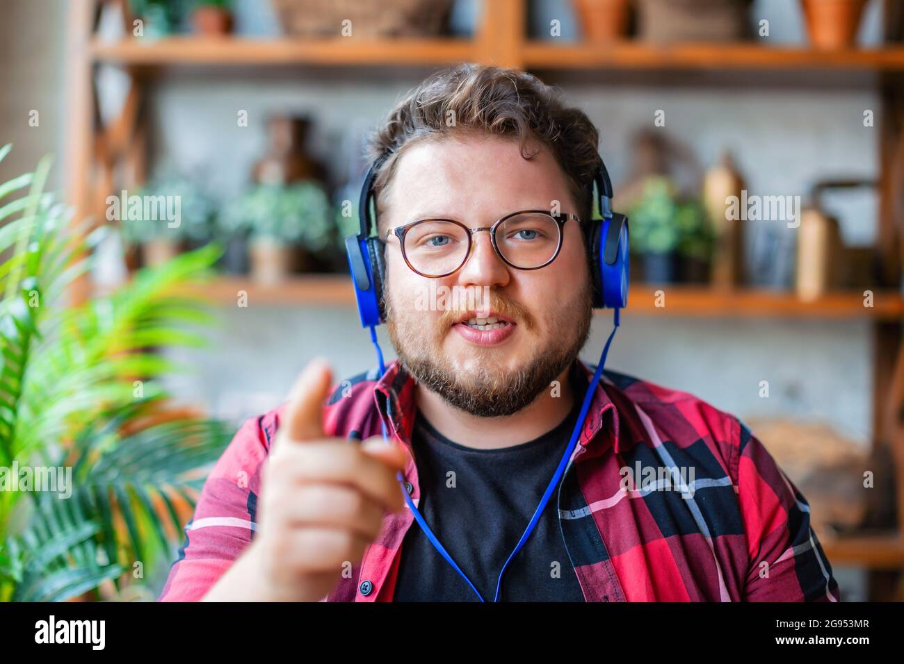 Photo of a young man in a blue headphones or headset during online video call. Online meeting with friends or relatives. He looking at camera and gest Stock Photo