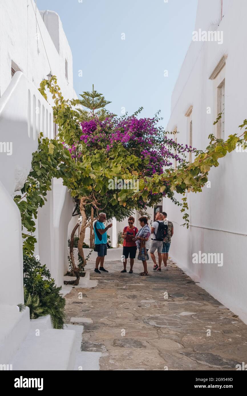 Ana Mera, Greece - September 24, 2019: People walking under flowering tree in Panagia Tourliani Monastery, a whitewashed church and monastery on Mykon Stock Photo