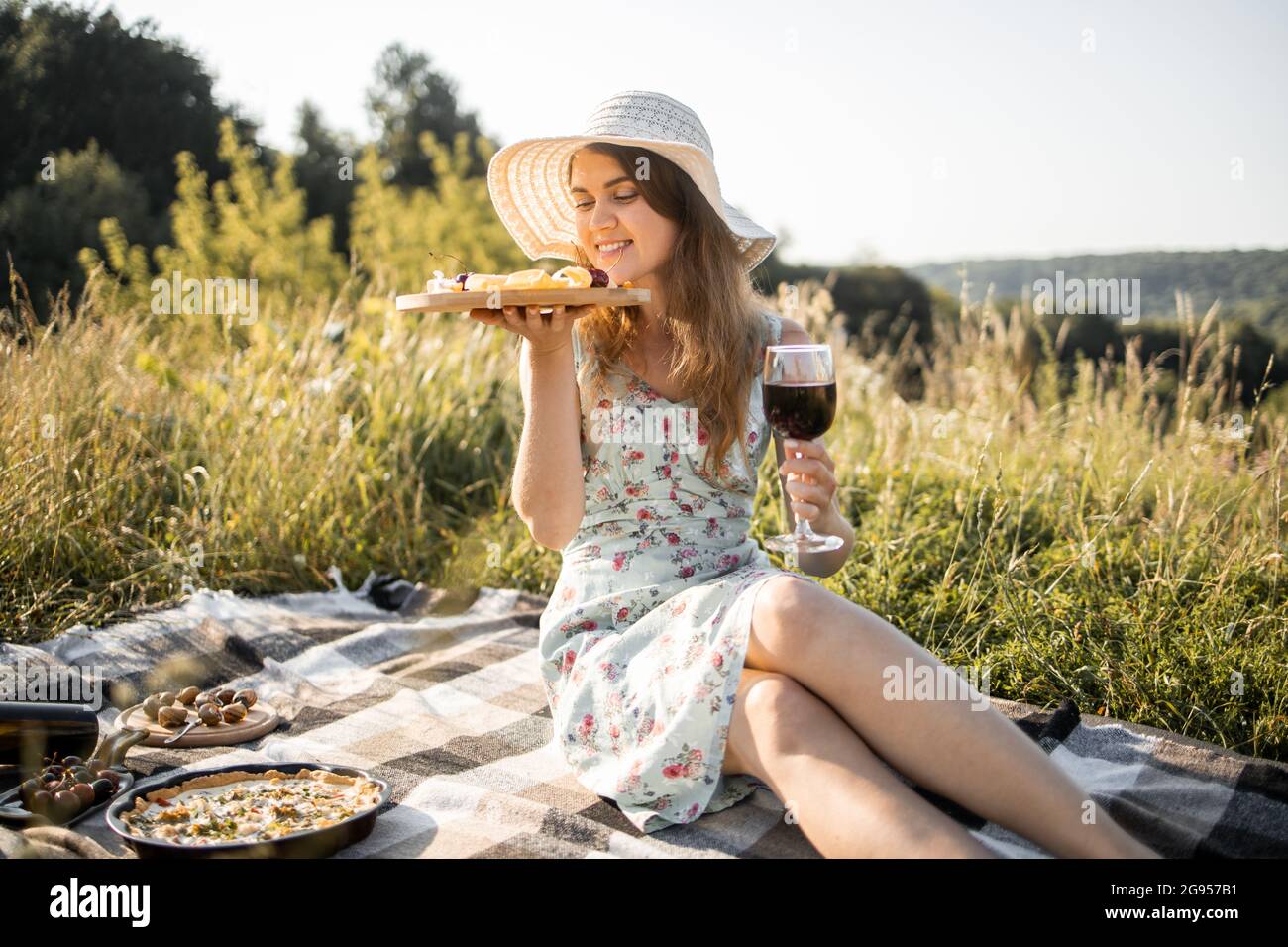 egetræ Uensartet reservedele Young girl in dress and stylish hat, sitting on the checkered plaid with  red wine and fresh fruits and cheese, enjoying her picnic at nature Stock  Photo - Alamy