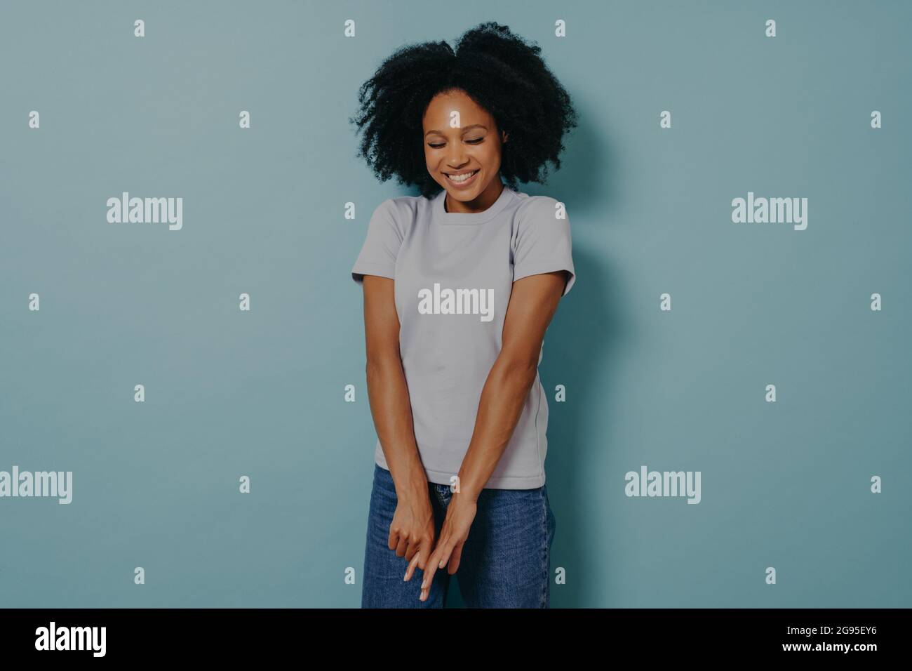 Young african lady looking down with with shy timid face expression, isolated over blue background Stock Photo