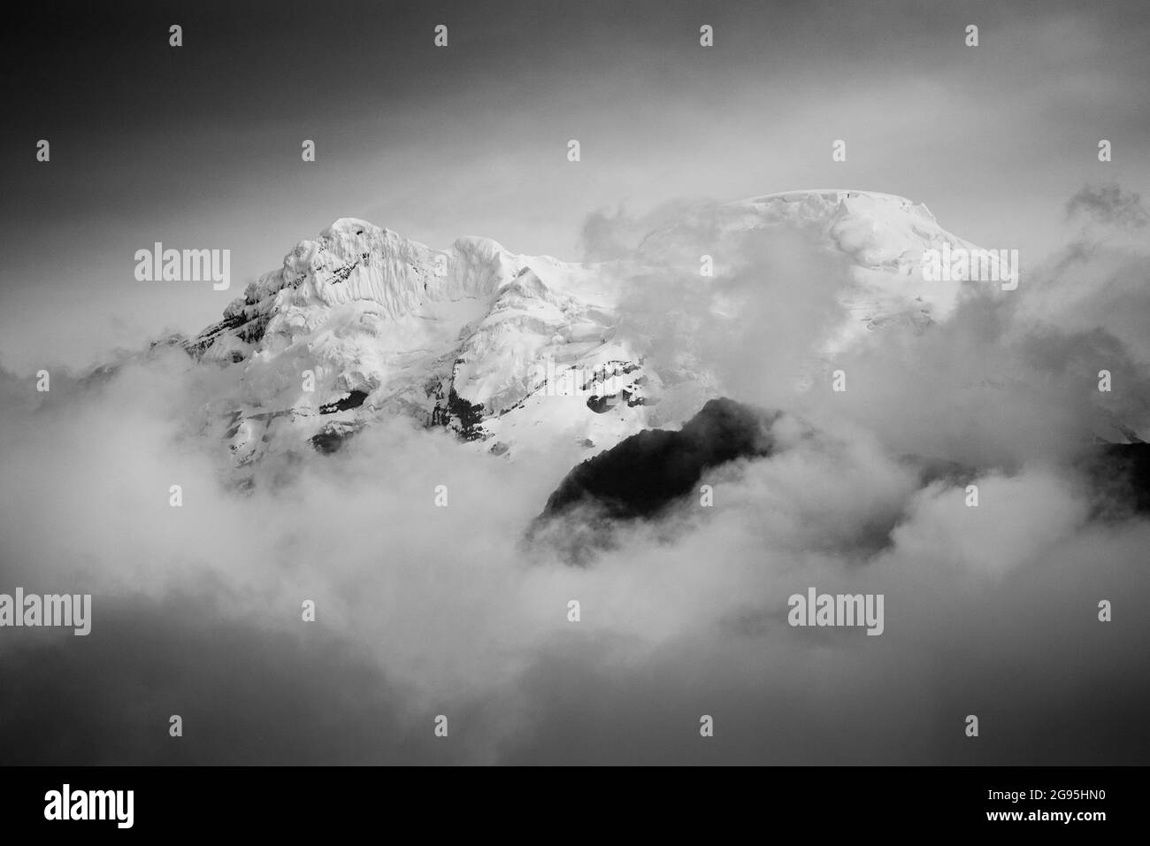 Grayscale shot of mountains covered in snow and clouds Stock Photo