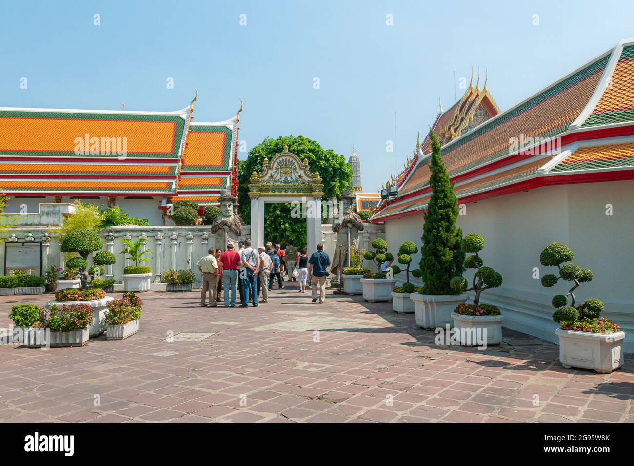 Tourists entering a gate guarded by large imposing Farang Guardian statues in the Wat Pho Wat Po temple complex in Bangkok in Thailand in South East A Stock Photo
