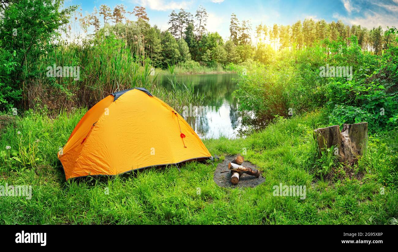 Orange tent on the river bank among green grass and trees Stock Photo