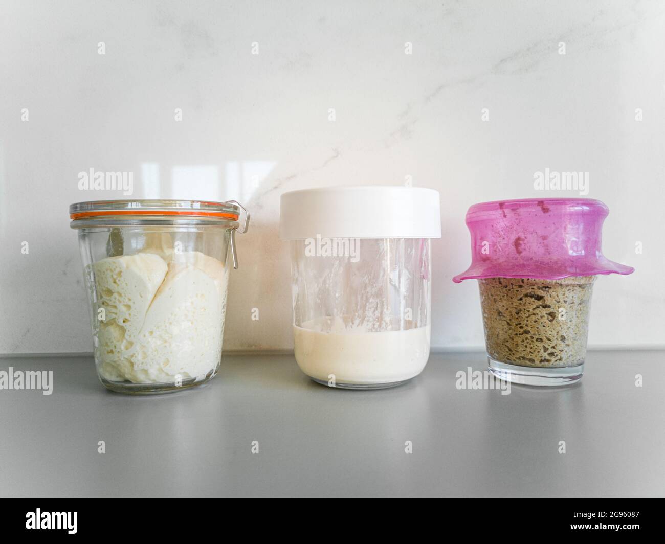 Three jars with different types of sourdough bread on table in kitchen Stock Photo