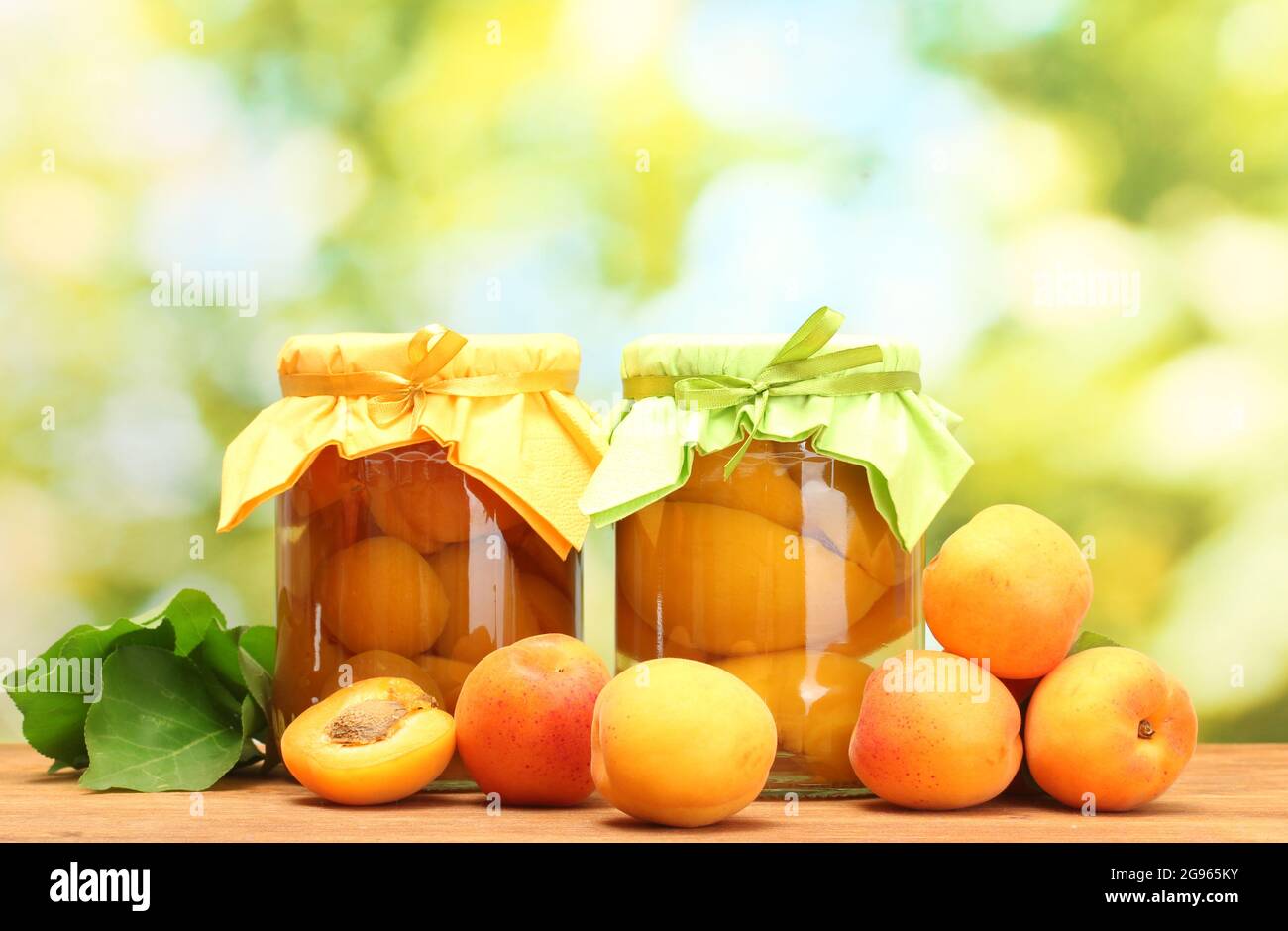 canned apricots in a jars and sweet apricots on wooden table on green
