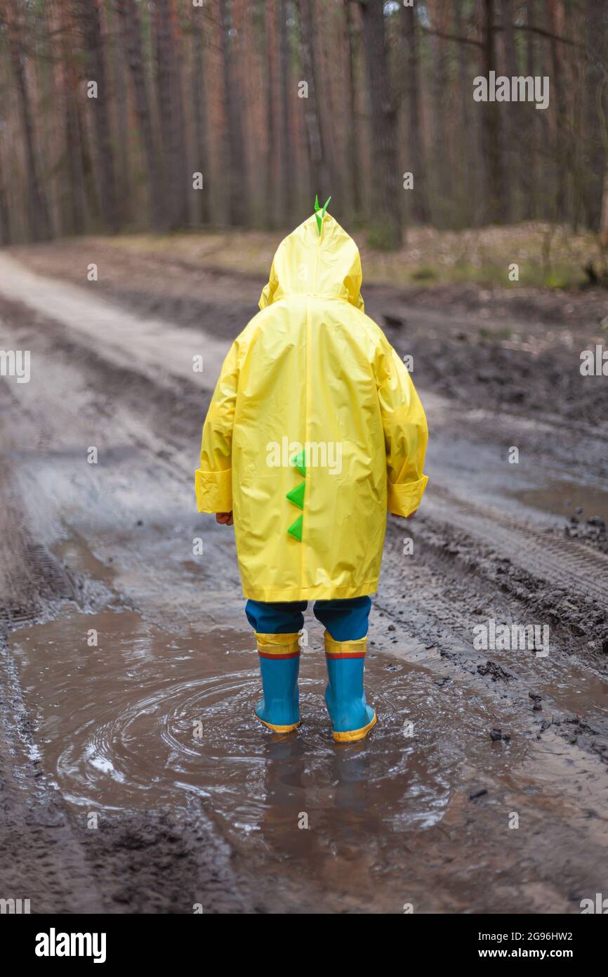 Child in a yellow raincoat walking in a puddle in rubber boots, walking