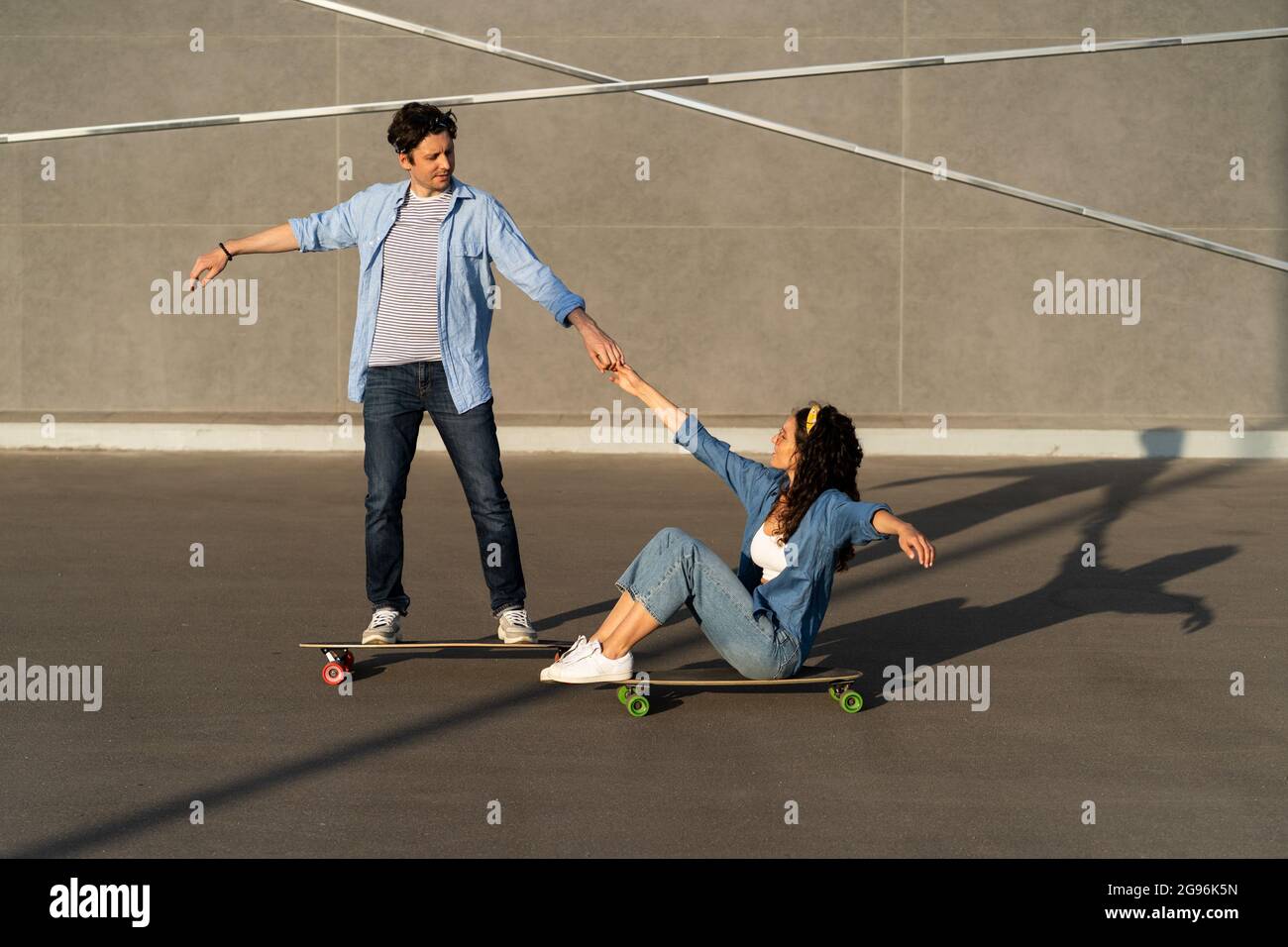 Active couple enjoy riding longboard together on summer city street. Man teach woman skateboarding Stock Photo