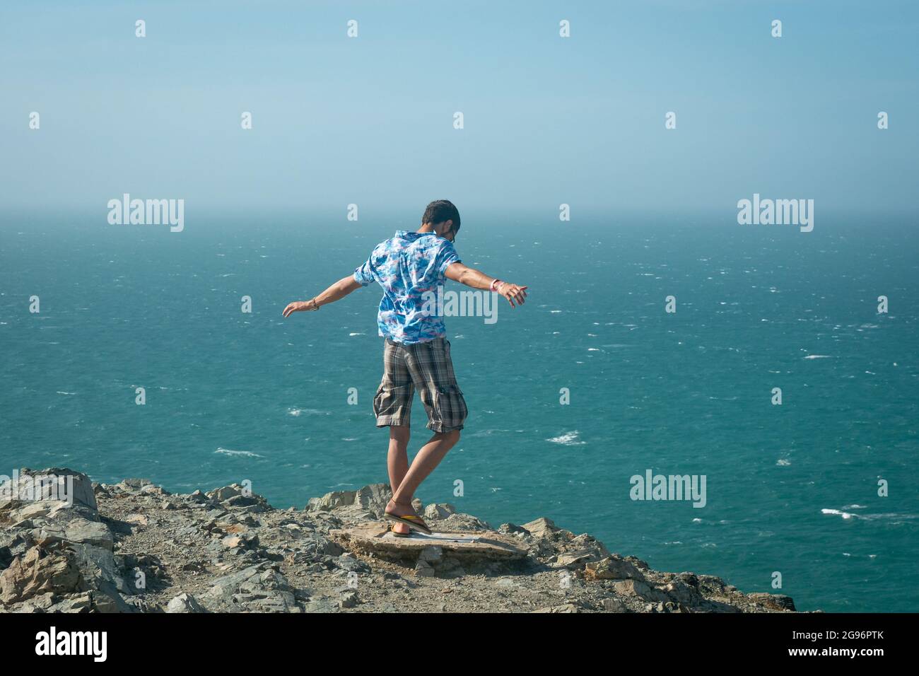 Young Latin Man on the Precipice of a Mountain Overlooking the Sea in the Desert in Uribia, La Guajira, Colombia Stock Photo