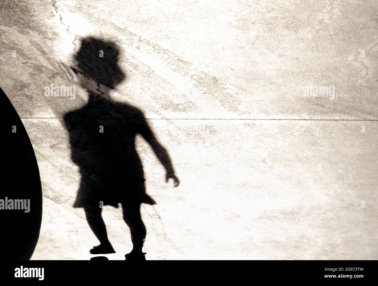 Blurry shadow silhouette of a little girl wearing a hat while walking alone on a summer day Stock Photo