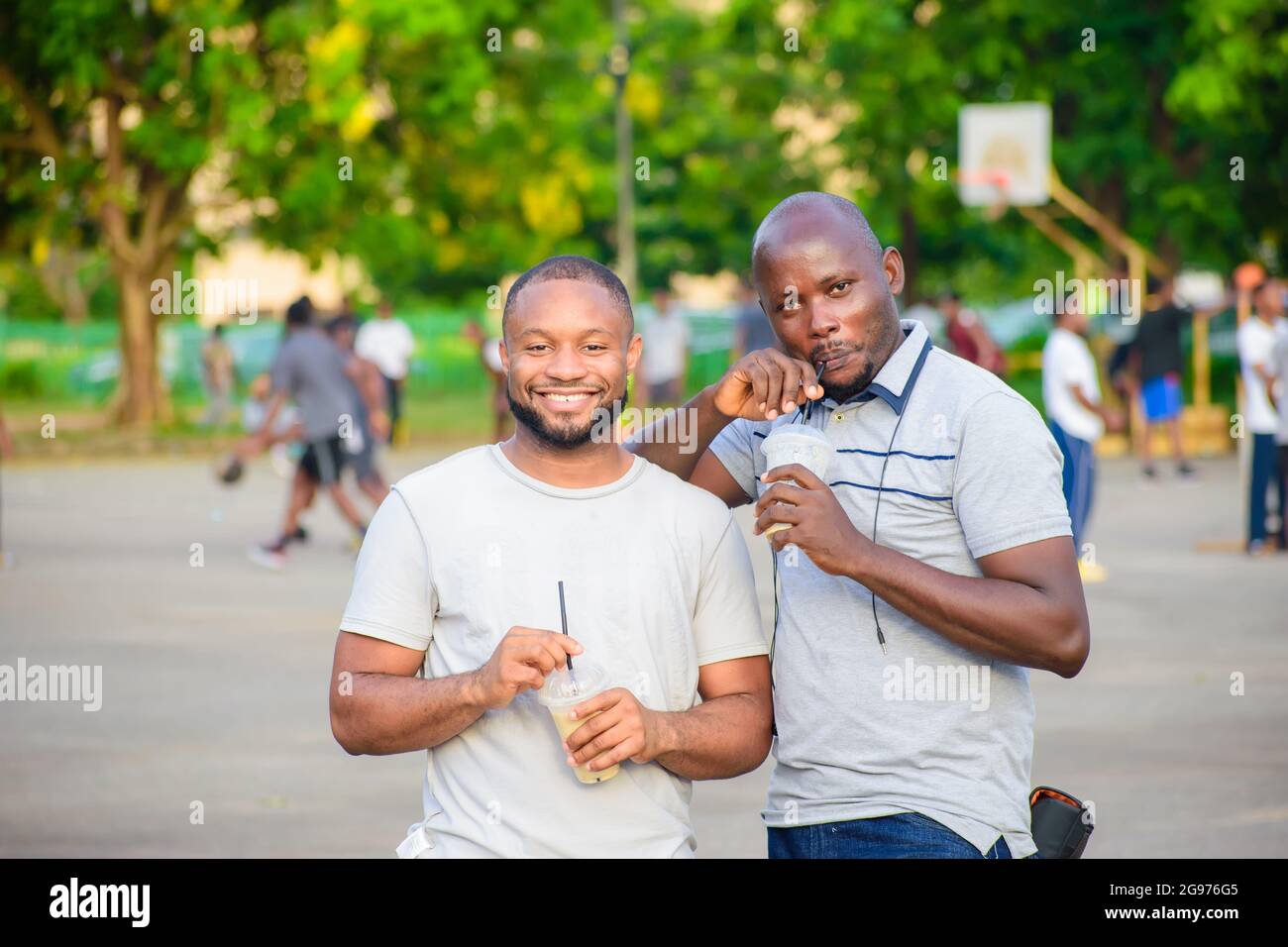 two male African friends standing and joyfully drinking fruit juice in an outdoor park in their leisure time Stock Photo