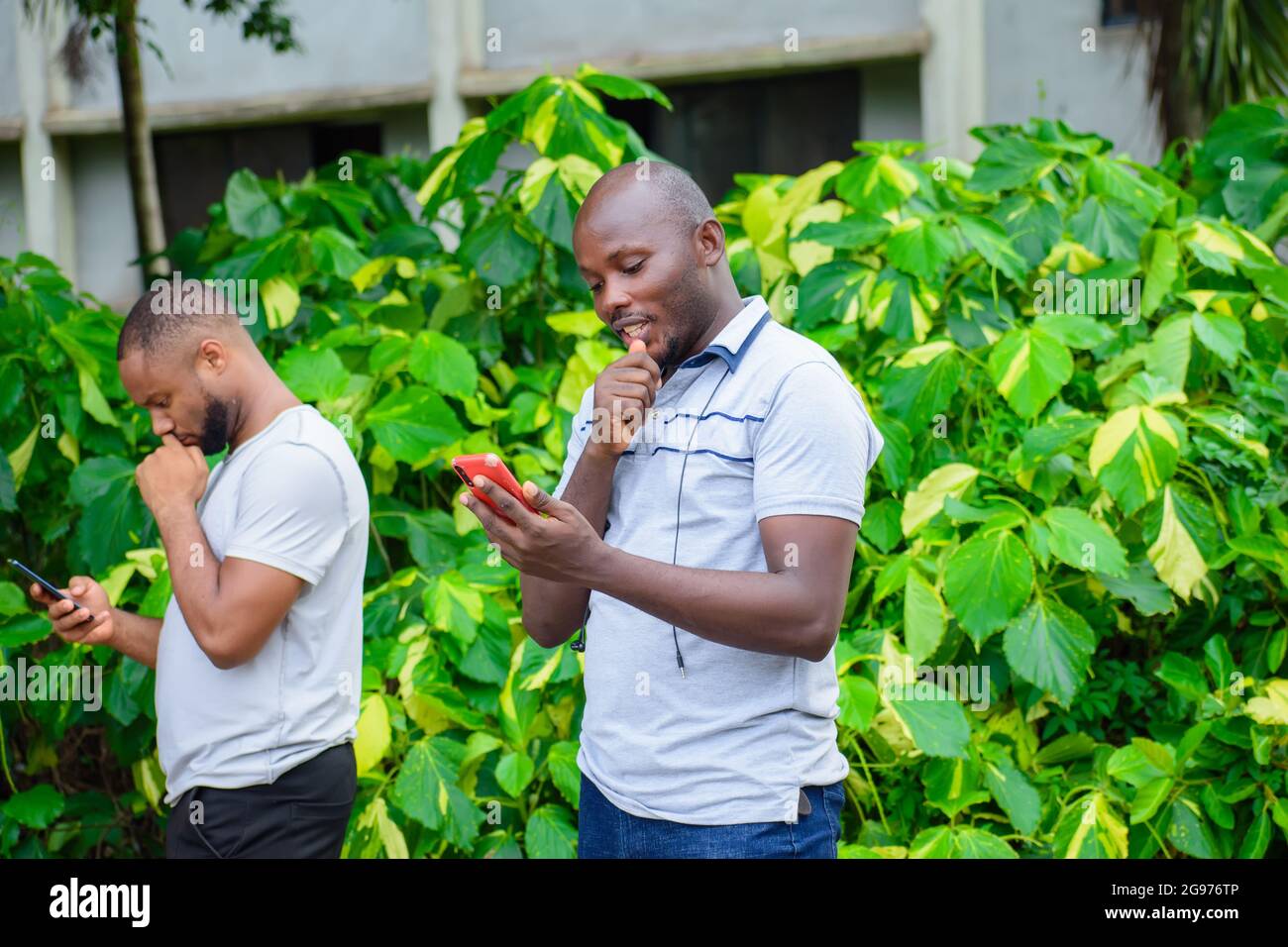 two African guys or men holding smart phones with different thoughtful and facial expression Stock Photo