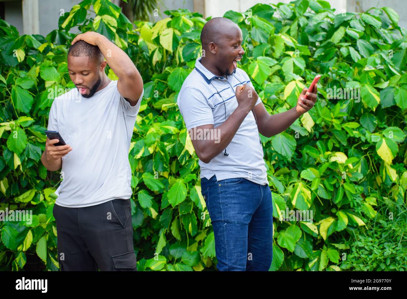 two African guys or men holding smart phones with different thoughtful and facial expression Stock Photo