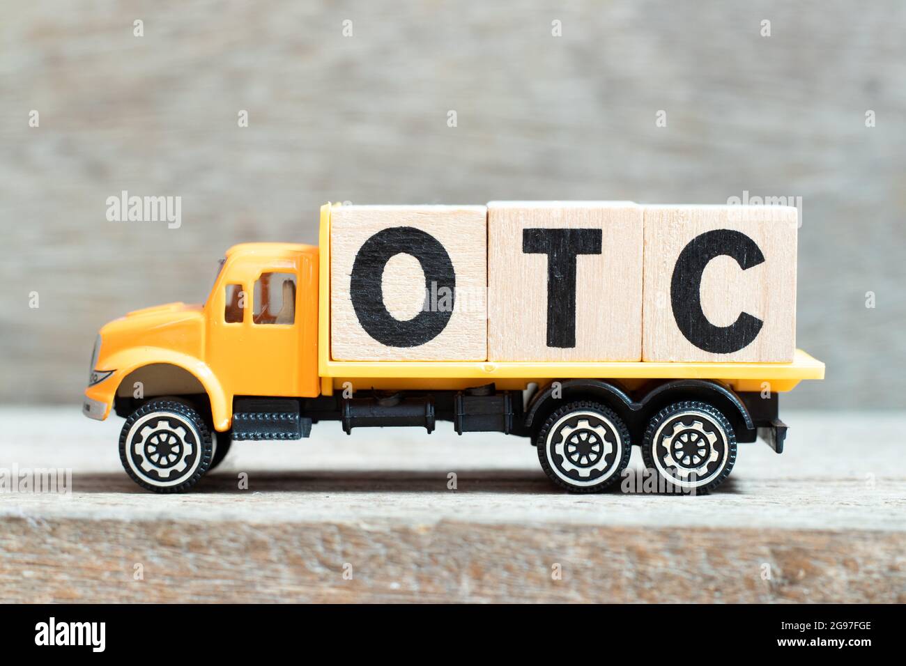 Toy truck hold alphabet letter block in word OTC (Abbreviation of over the counter) on wood background Stock Photo