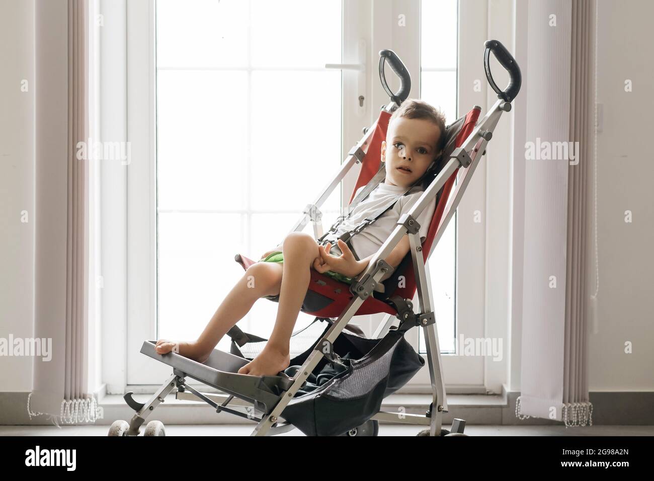 Boy with with Cerebral Palsy in special chair going outside by the door. Accessibility for disabled people in prams. Stock Photo