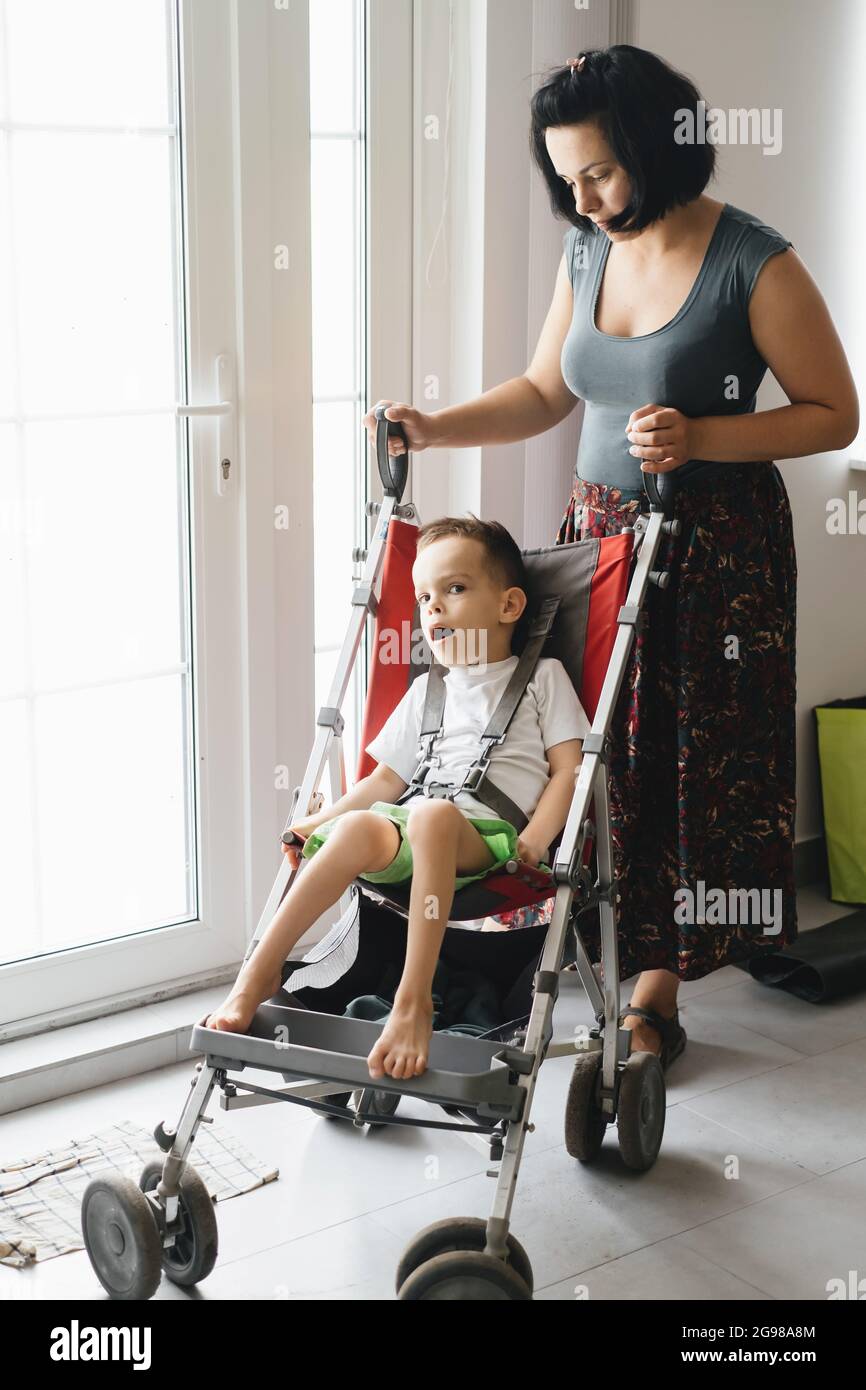 Mother with disabled child in big stroller. Accessibility of people in wheelchairs and prams. Woman going though the door, Children with Special Needs Stock Photo